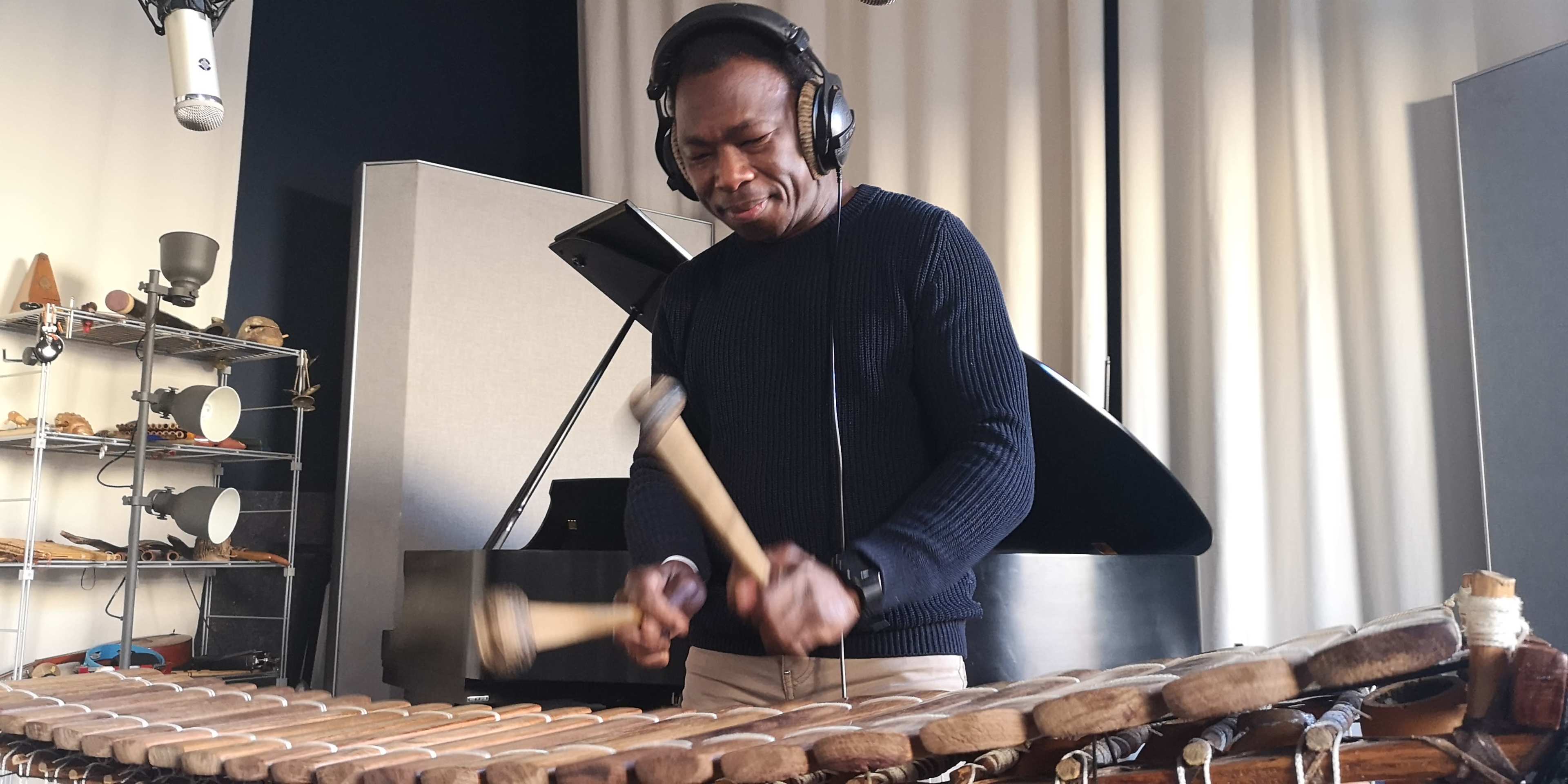 A musician plays a wooden xylophone while wearing headphones in a studio setting.