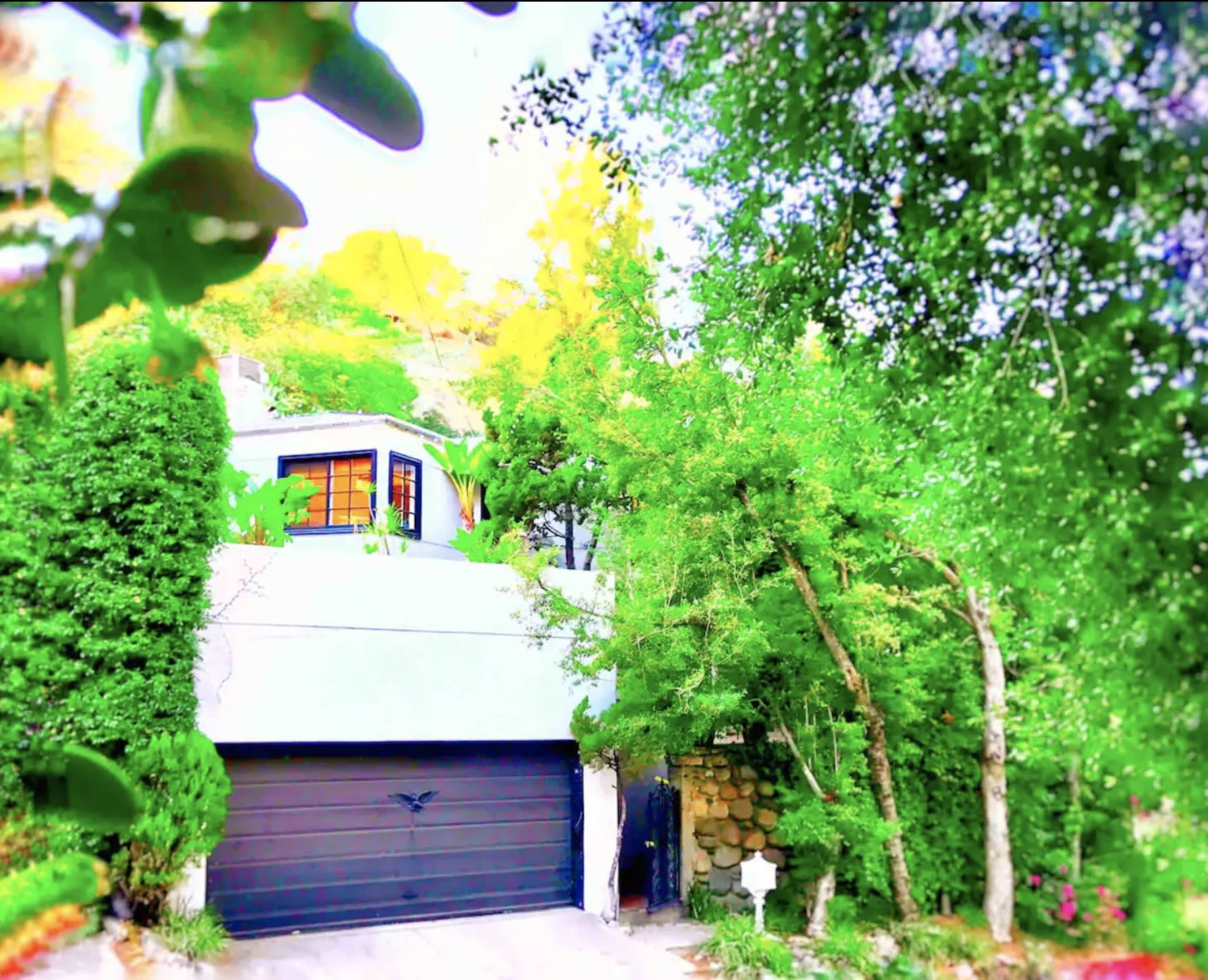 A modern house with a flat roof is set amidst lush greenery, featuring a two-car garage and large windows.