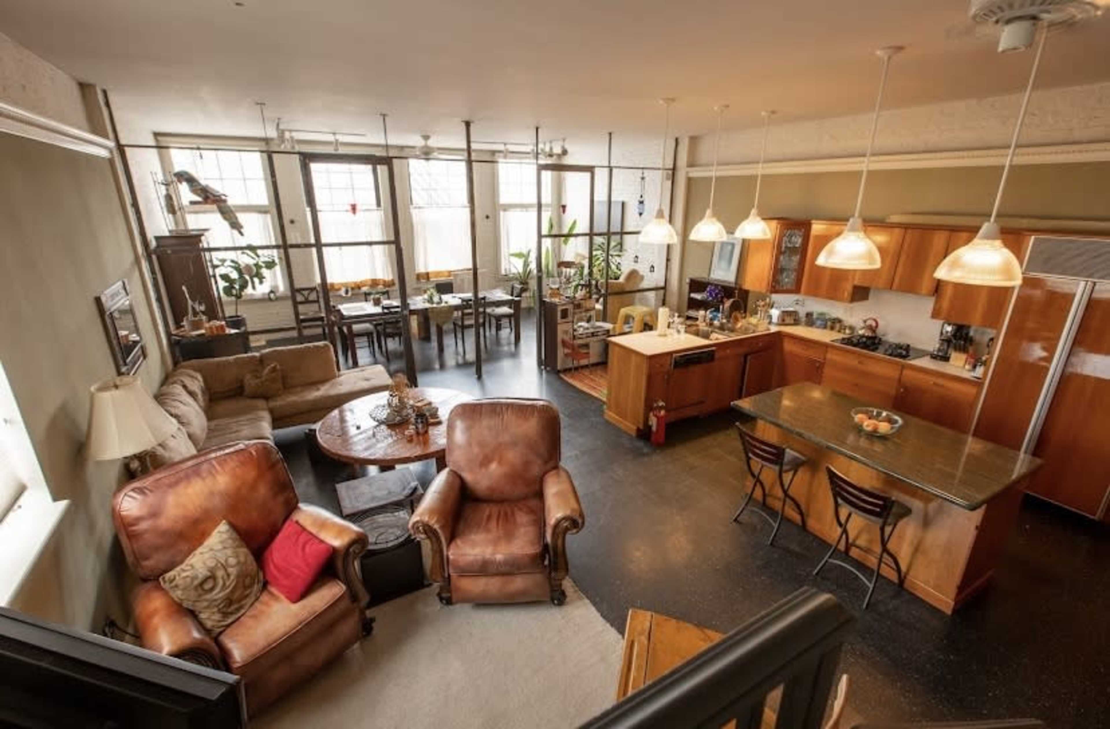 A spacious, open-concept loft with a kitchen, living area, and dining space, featuring large windows and modern furnishings.