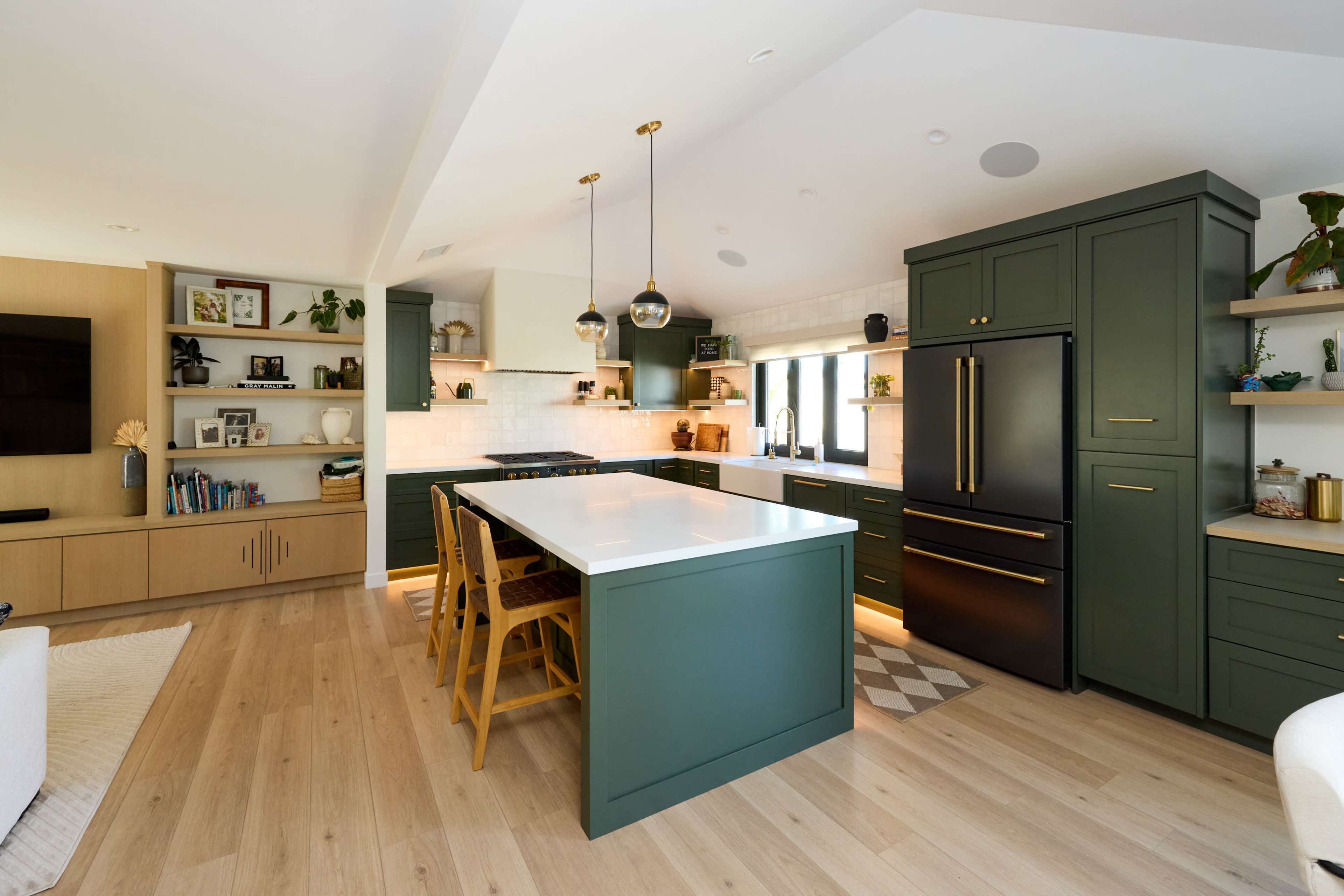 The image shows a modern kitchen featuring green cabinetry, a white countertop, wooden flooring, and a dining area with yellow chairs.
