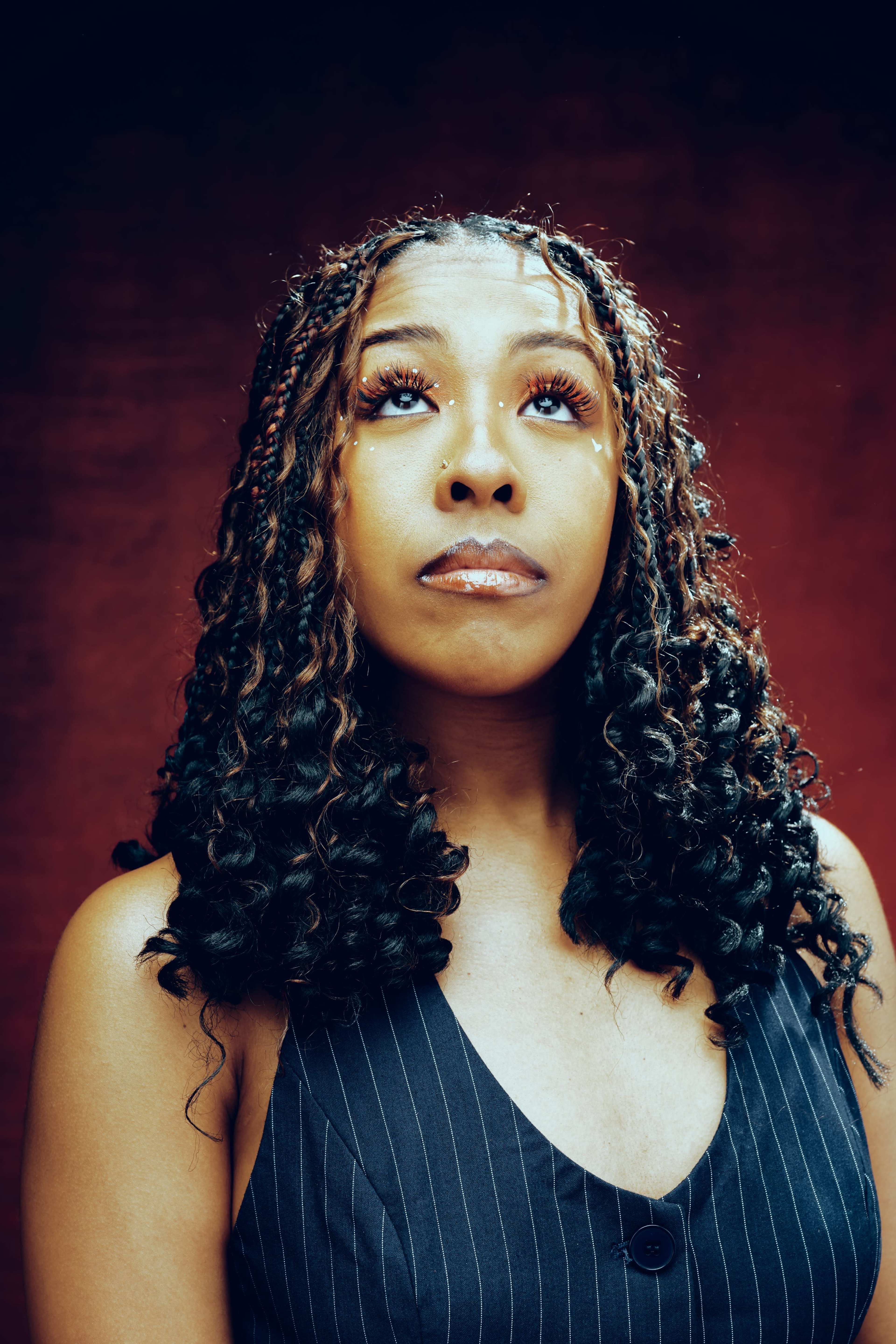 A woman with curly hair gazes upwards against a red background.