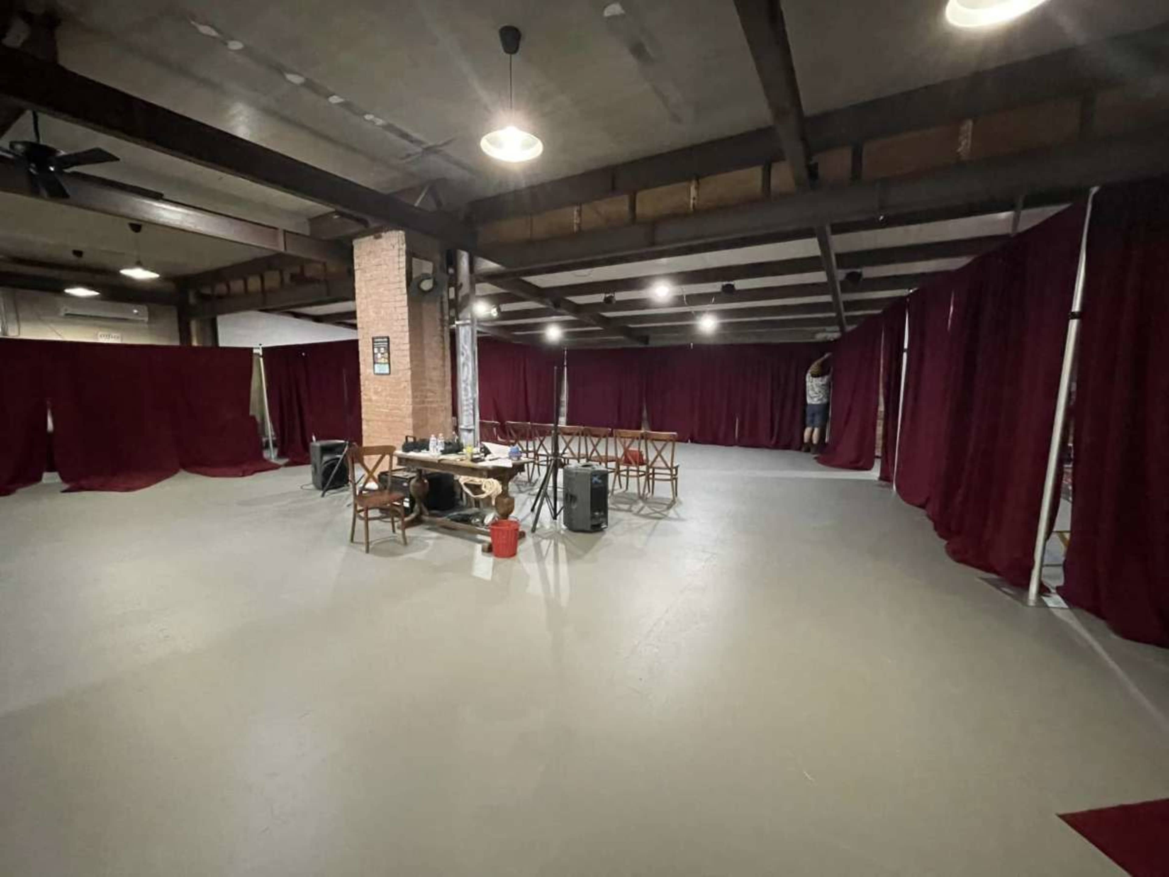 The image shows a spacious indoor area with a gray floor, several tables, and burgundy curtains forming partitions.
