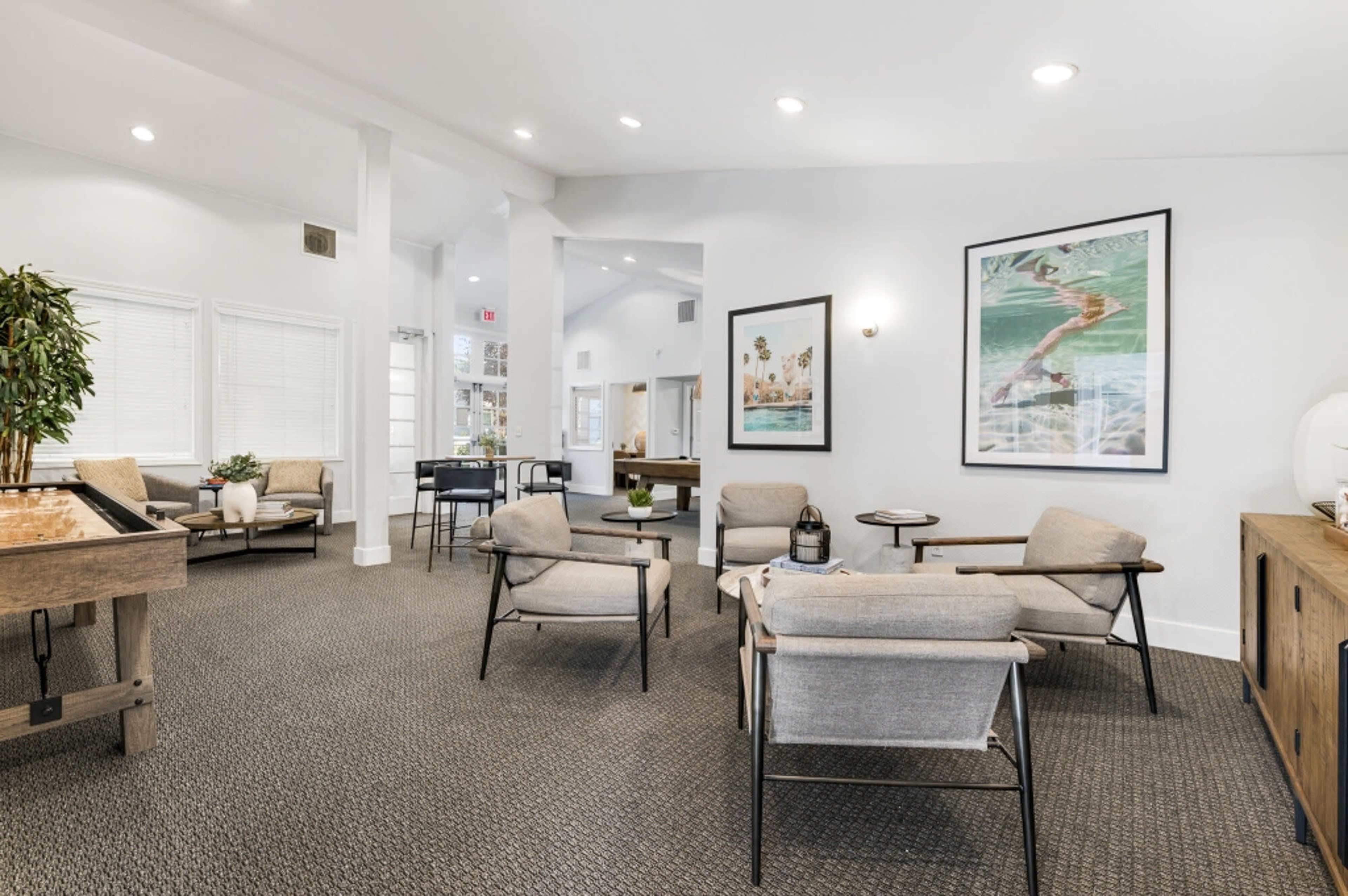 The image shows a modern lounge area with seating, artwork on the walls, and a tabletop game in a well-lit space.