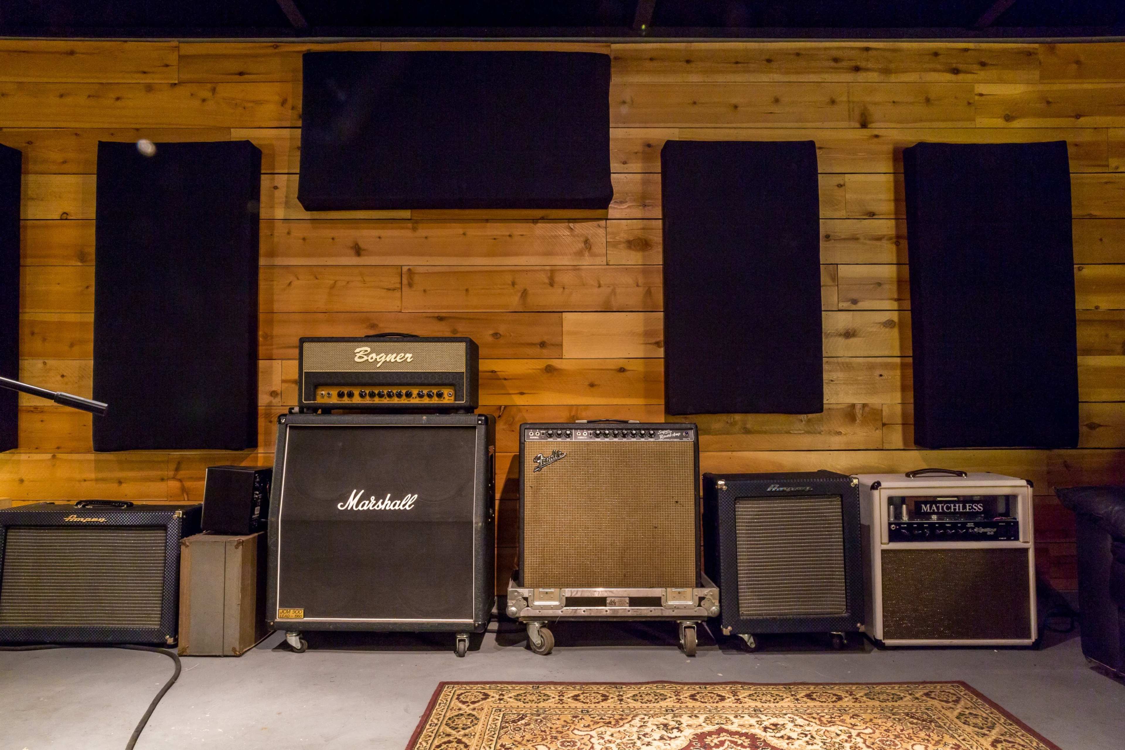 A wall of music amplifiers arranged on a wooden floor with acoustic panels mounted on the wall.