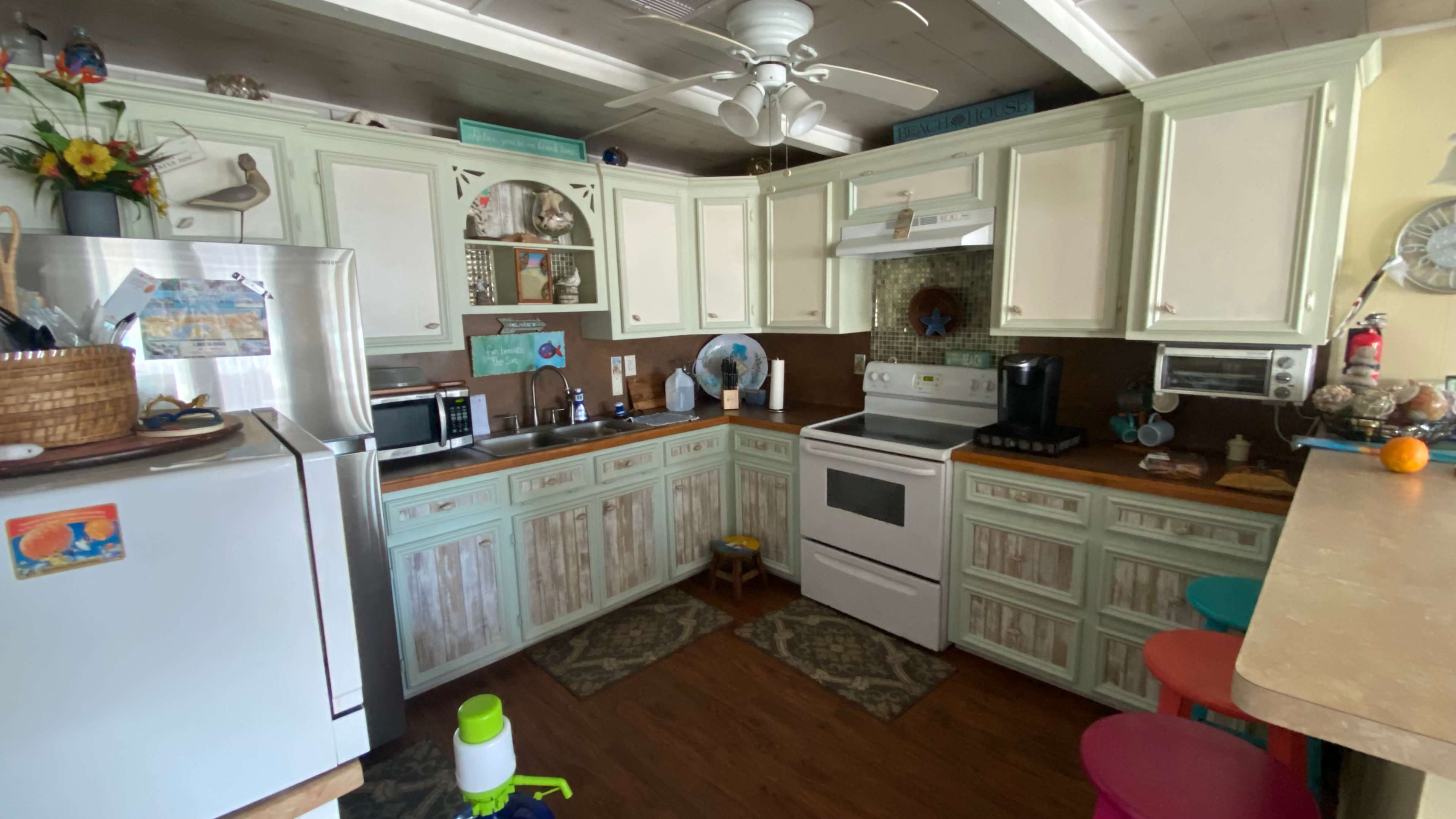 The kitchen features light green cabinets, a white stove, and an arrangement of appliances along the countertops.