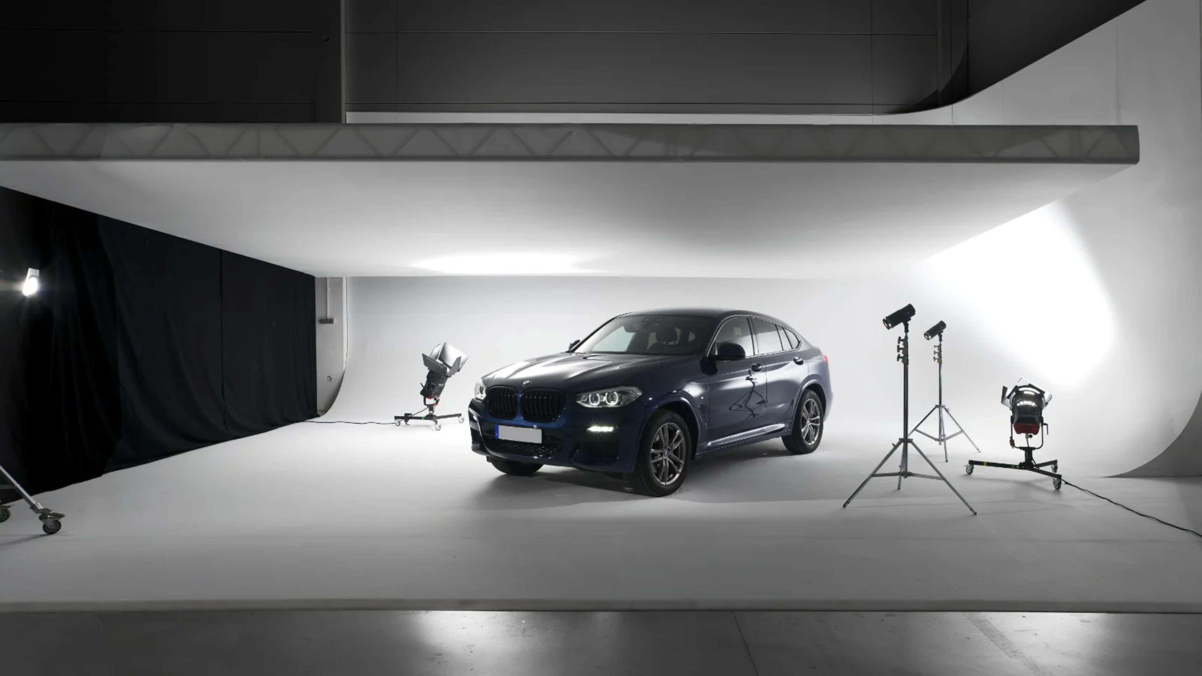A dark blue BMW is positioned on a white studio backdrop, illuminated by various lighting equipment.