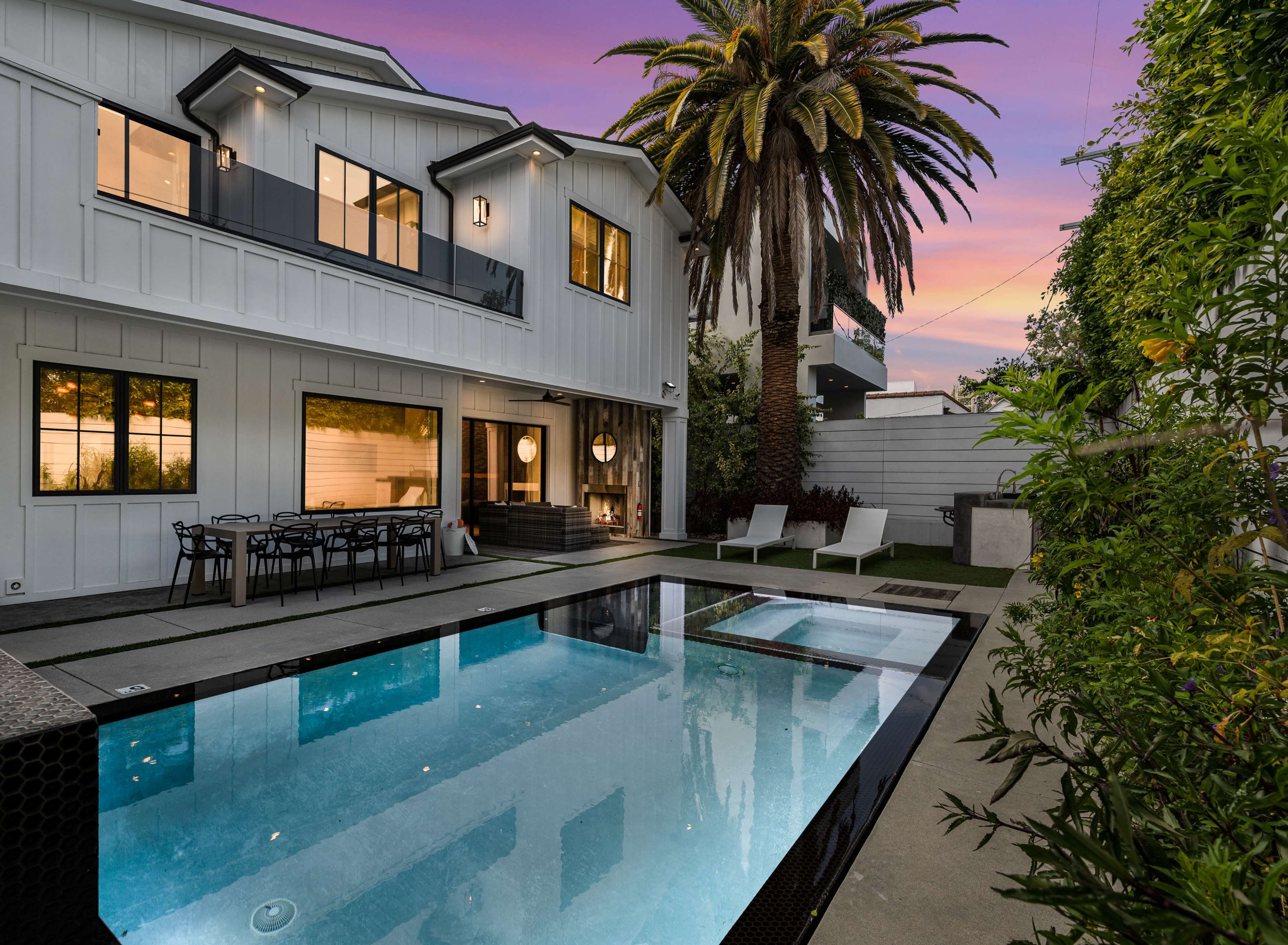 A modern house with a pool and palm trees is set against a colorful sunset sky.