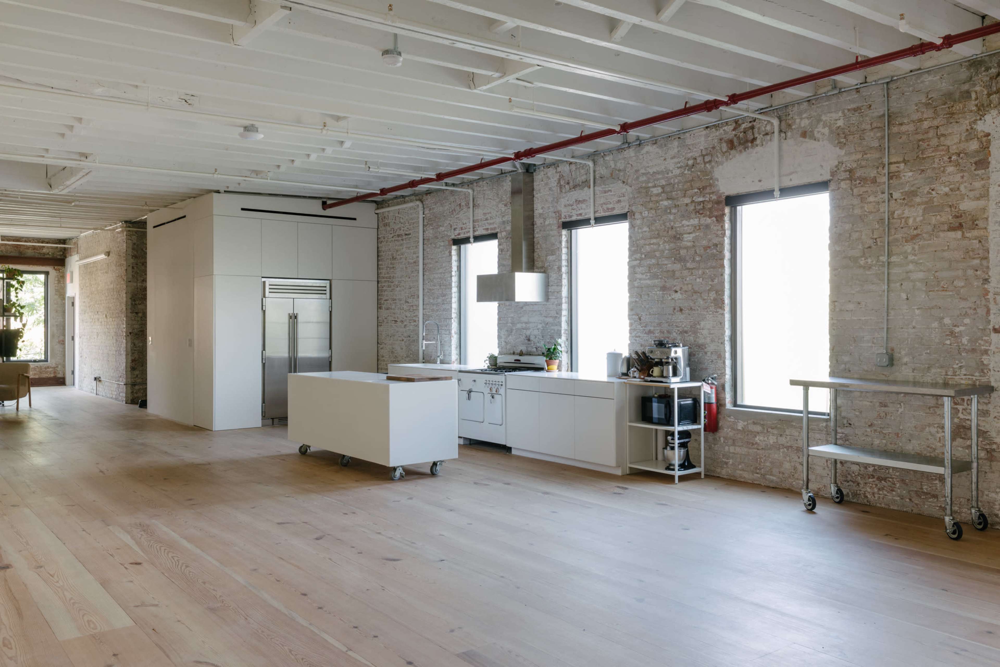 A spacious, modern kitchen with white cabinetry, an island on wheels, and large windows allowing natural light to fill the room.