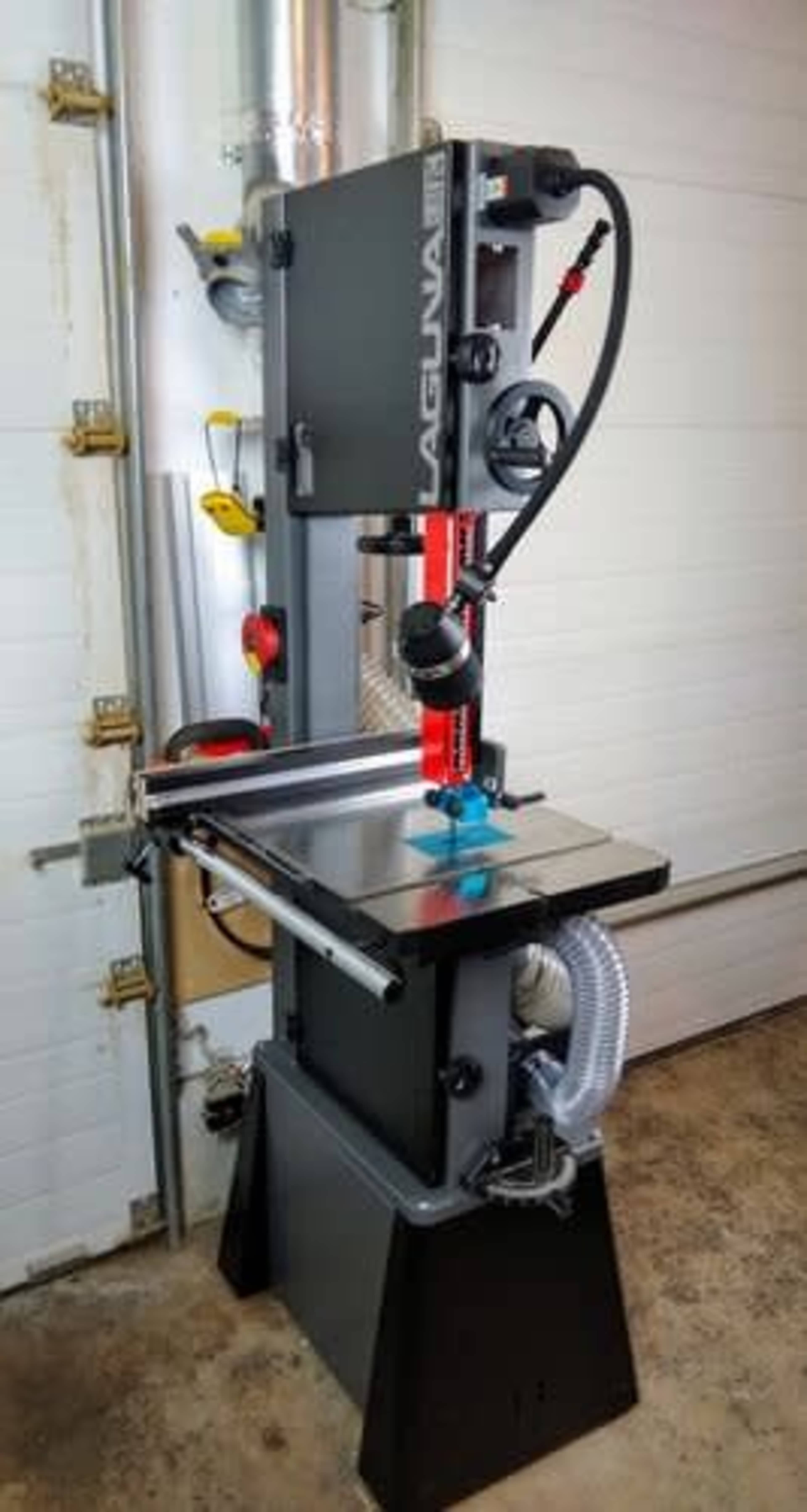 A Laguna bandsaw set up in a workshop, featuring a vertical cutting blade and a large flat table with a dust collection system.