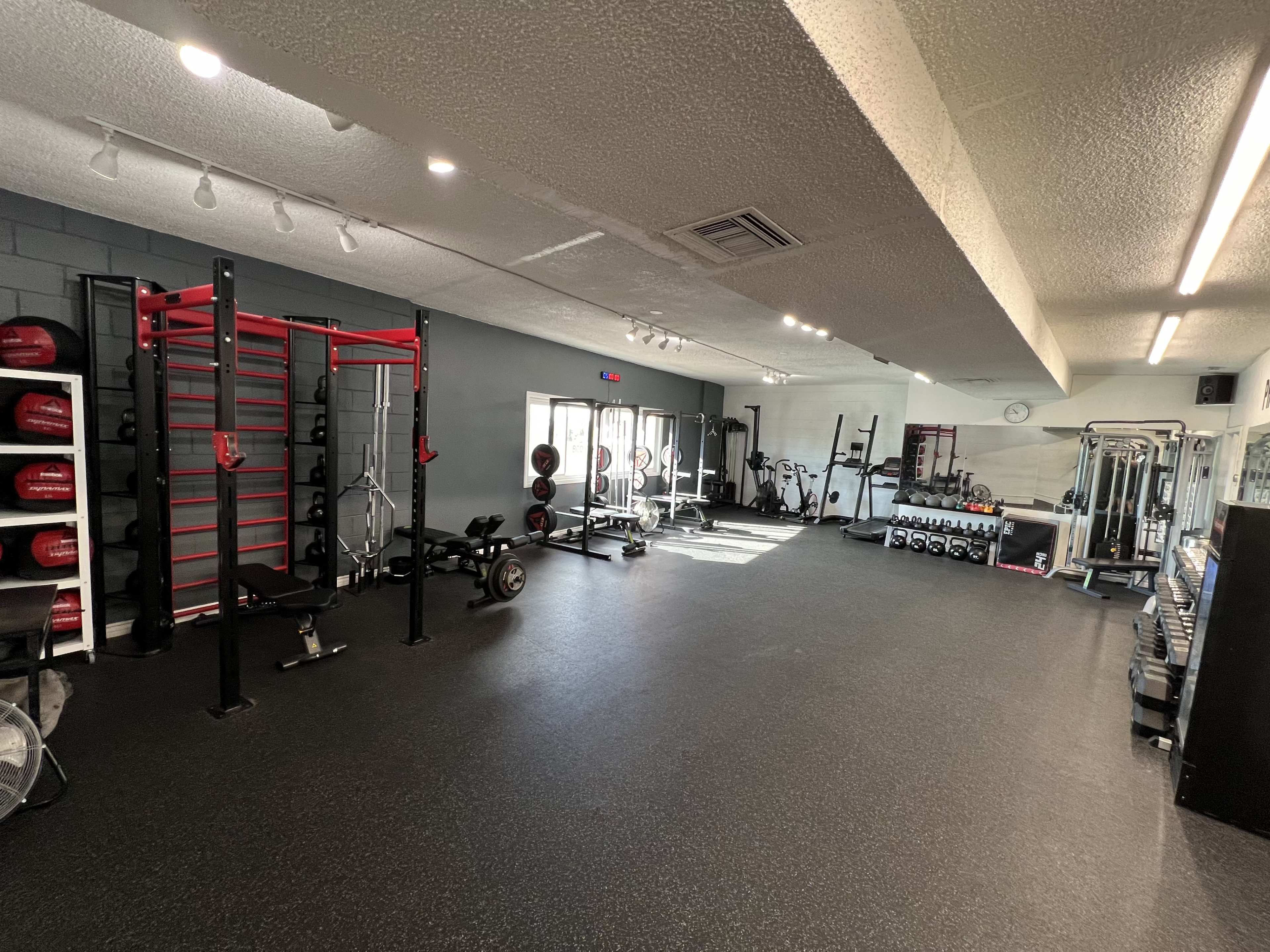The image shows a well-equipped gym featuring various strength training equipment, weight racks, and exercise machines in a spacious layout.