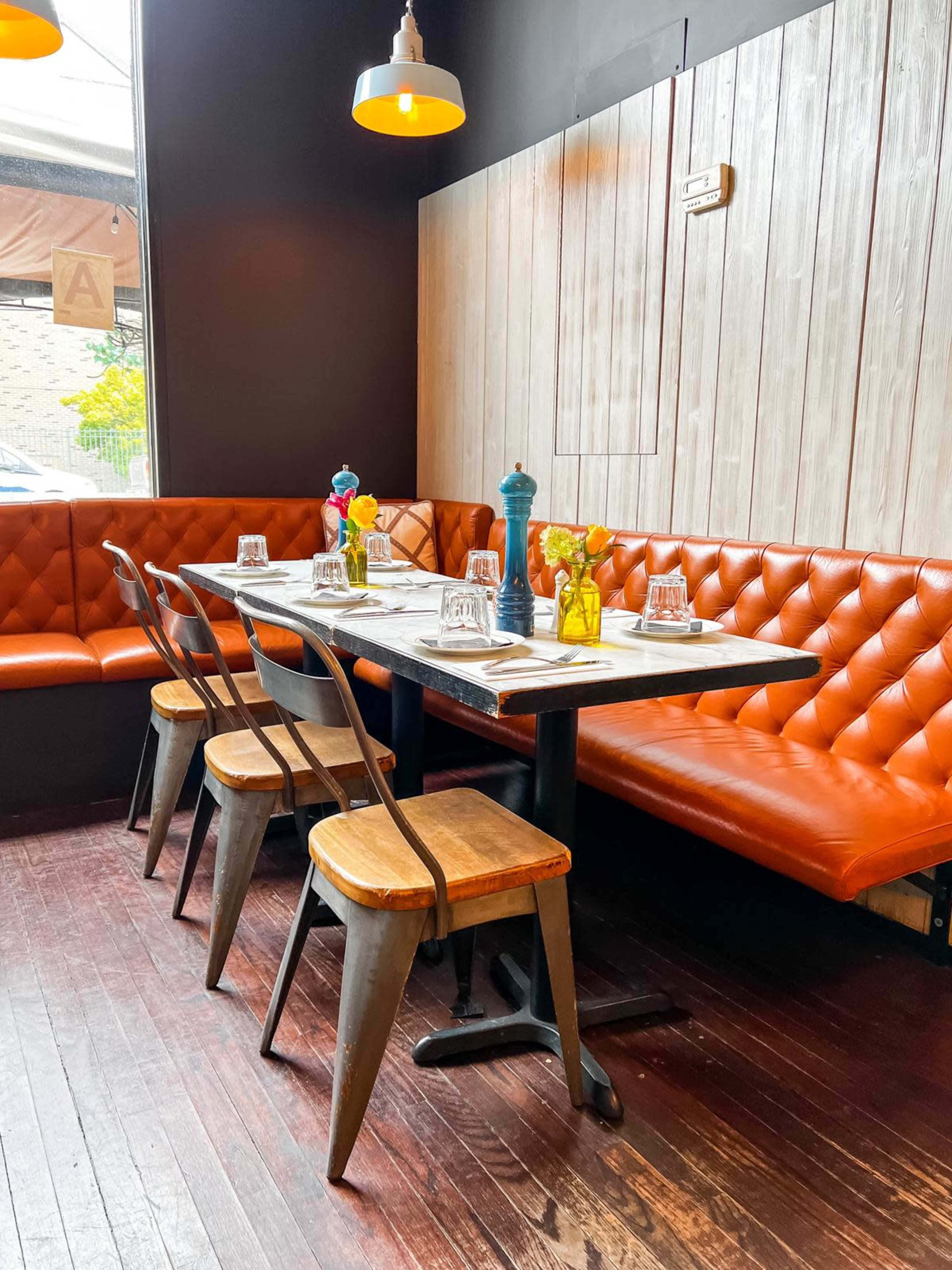 A dining area features a wooden table surrounded by metal and wooden chairs, with a tufted orange banquette along the wall.