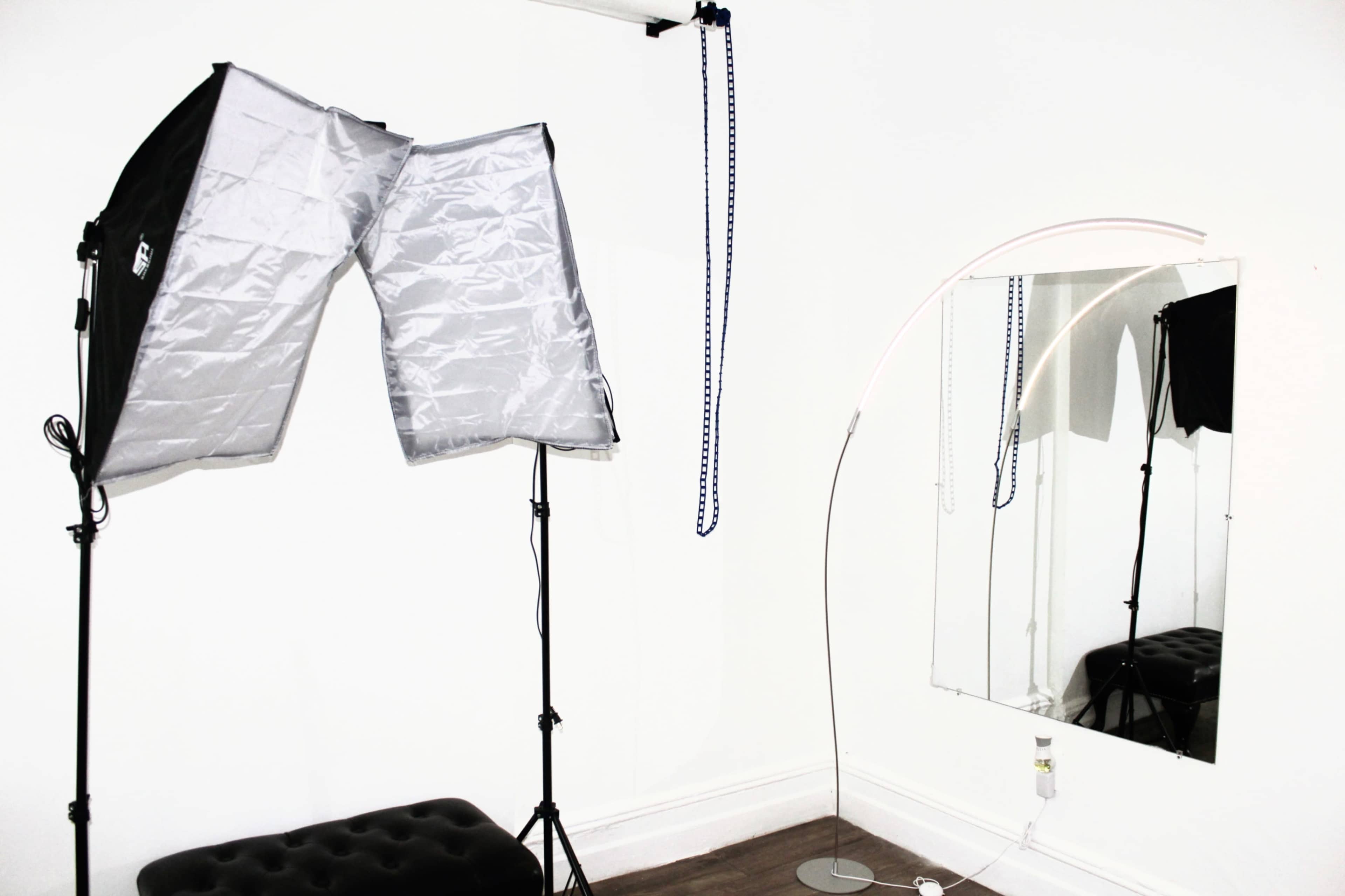 A corner of a studio featuring a lighting setup with softboxes, a floor lamp, and a wall-mounted mirror.