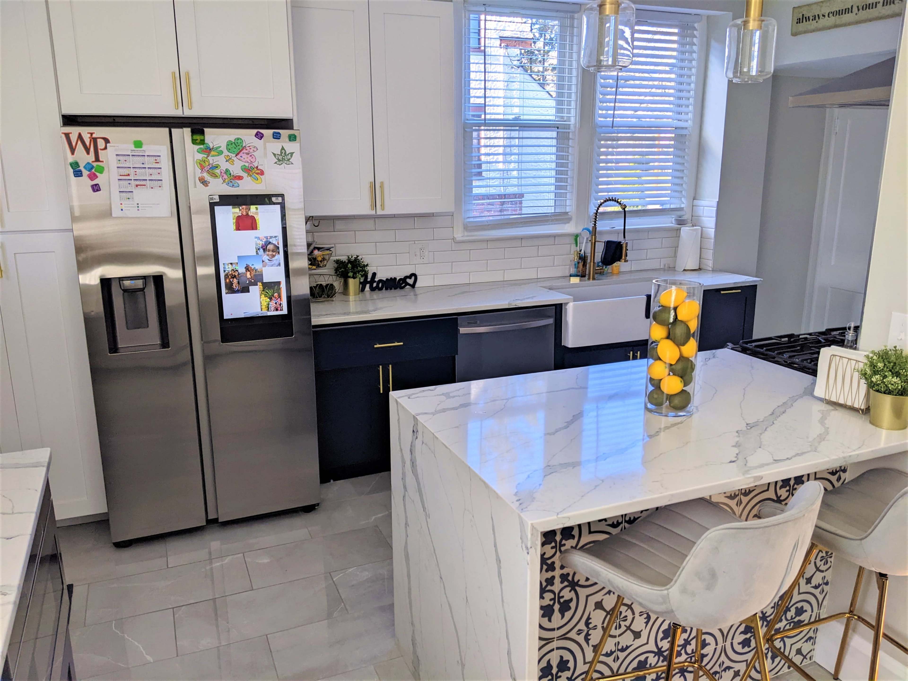 A modern kitchen with a stainless steel refrigerator, a farmhouse sink, and a marble island featuring a vase of lemons.
