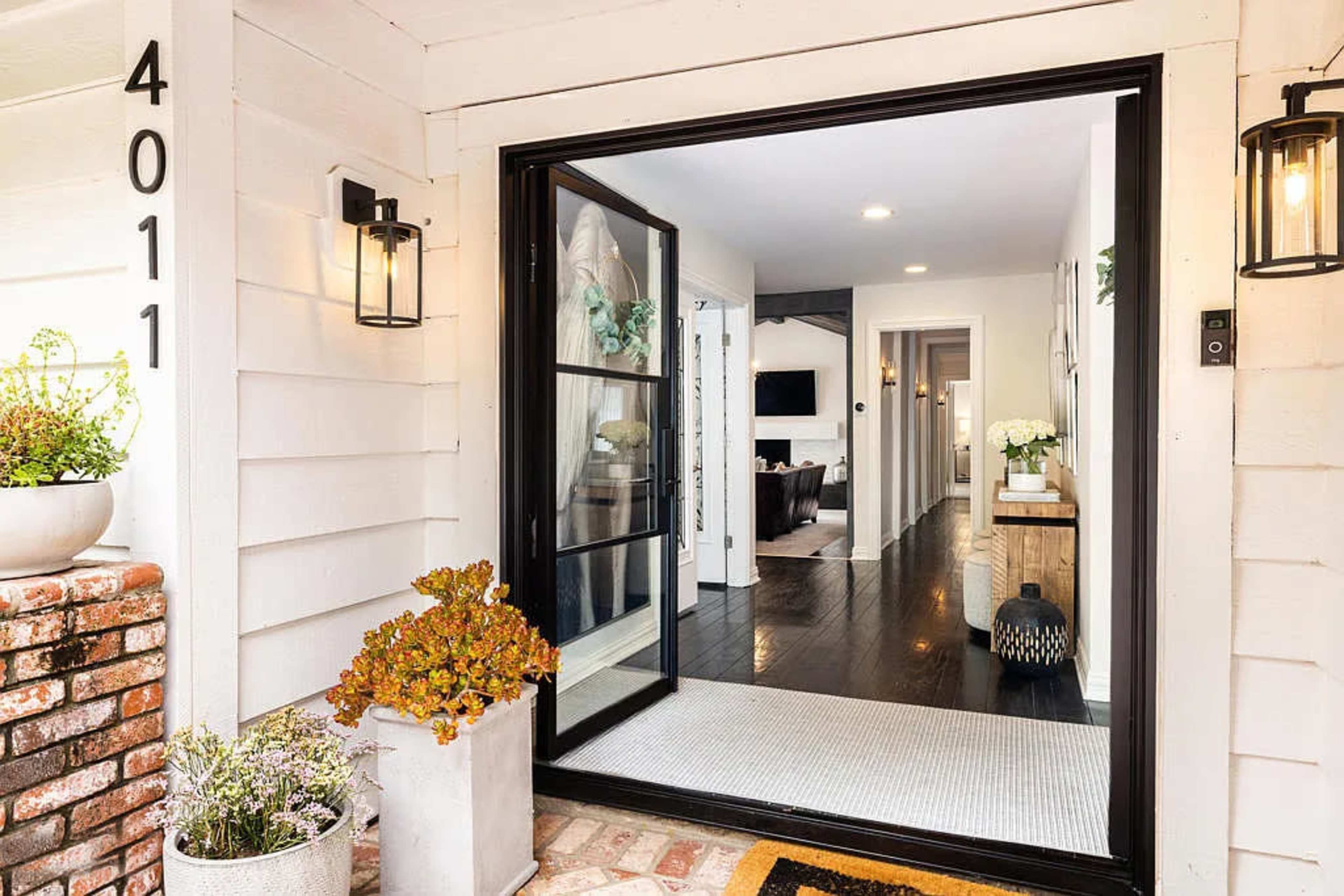 An inviting front entrance with a black-framed glass door leading into a well-lit hallway, featuring a view of a living area at the end.