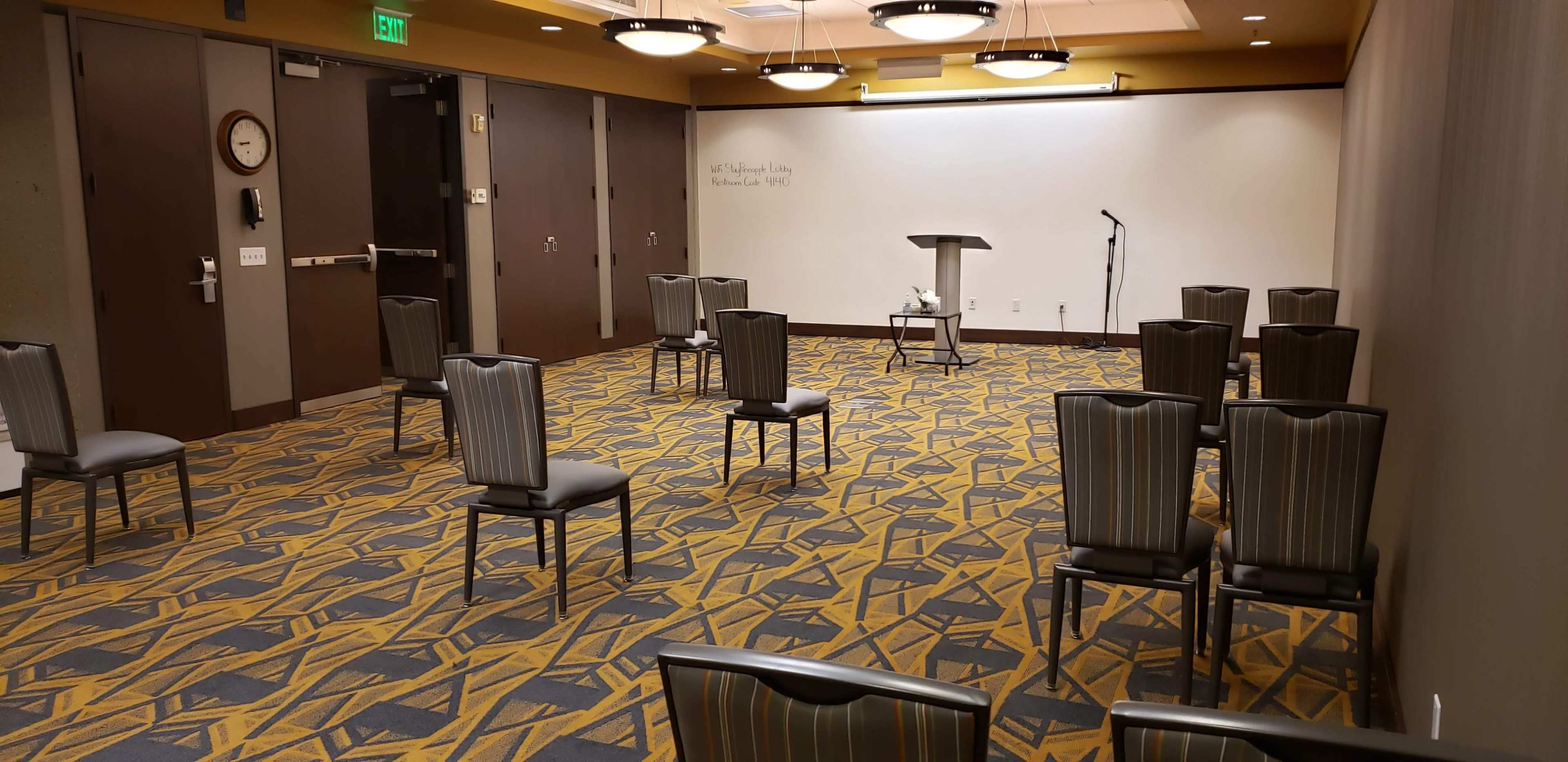 A sparsely arranged room features several chairs facing a podium and a microphone in front of a blank wall.