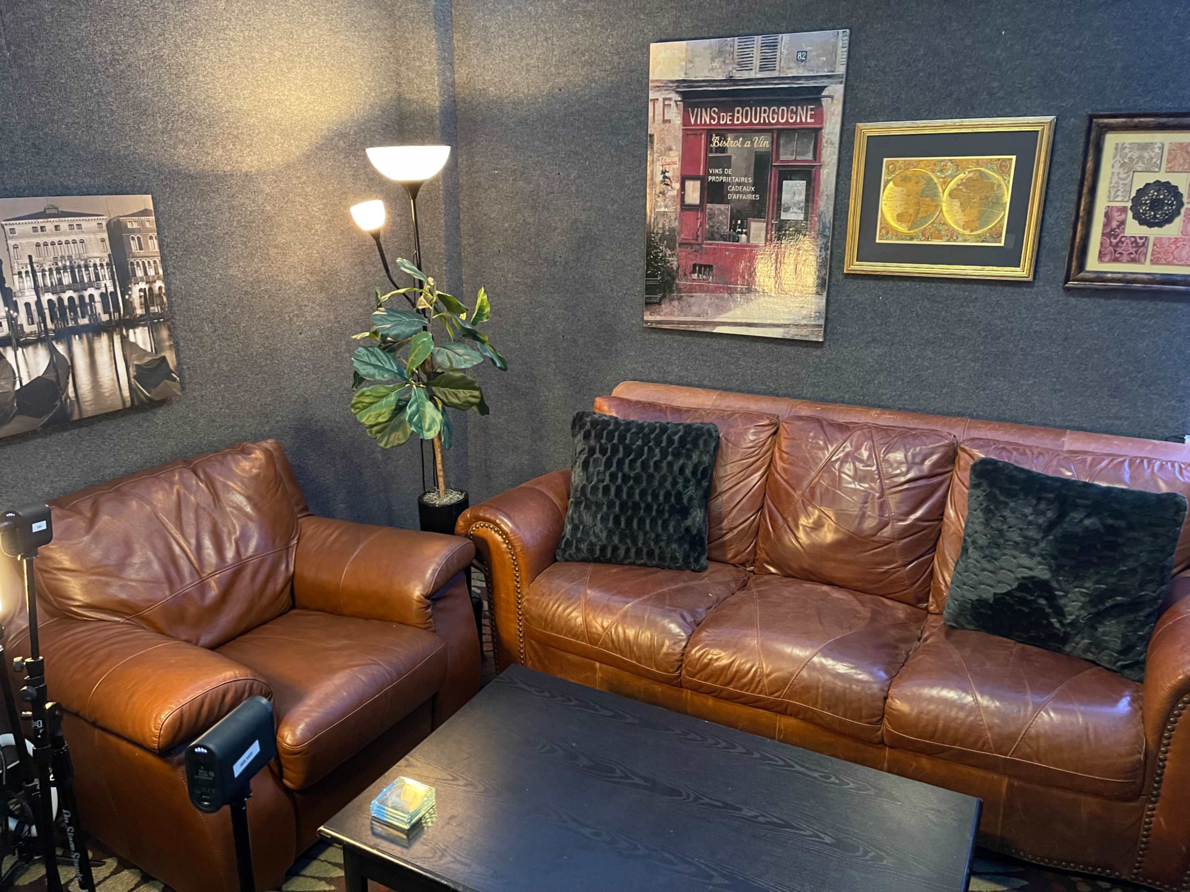 A cozy seating area with a brown leather sofa and an armchair, accompanied by a coffee table and art pieces on the walls.