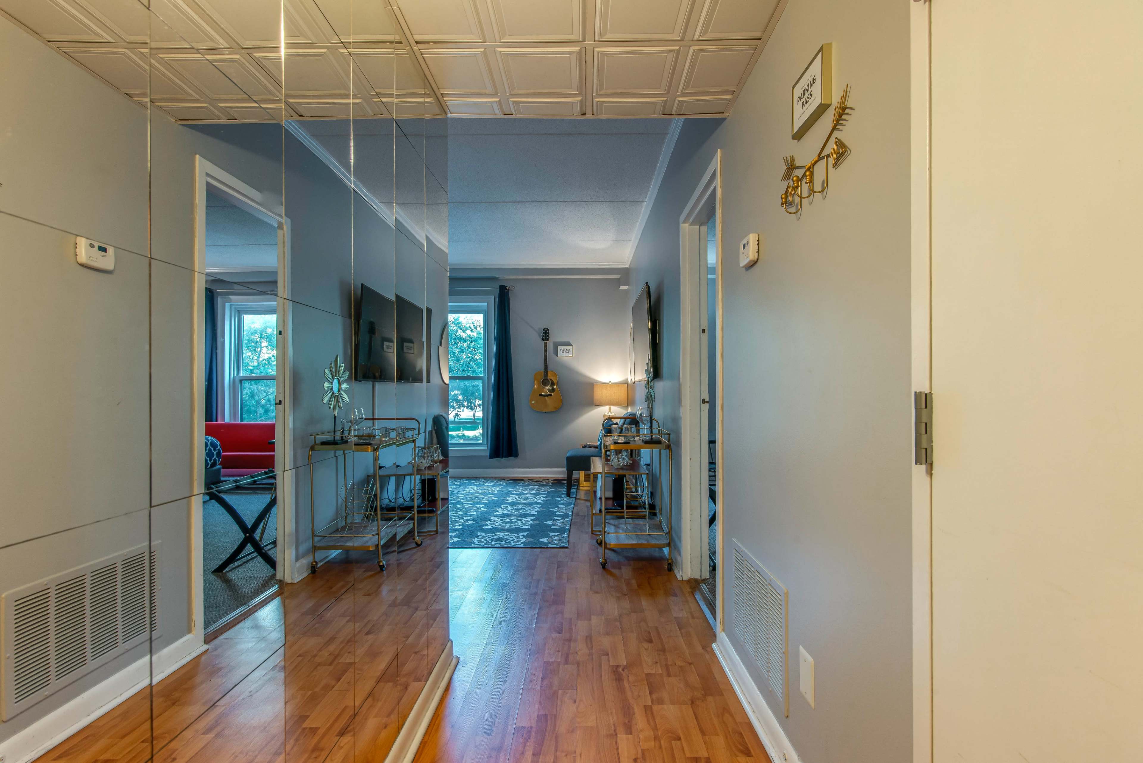A hallway with mirrored walls leading to a living area furnished with a guitar, a table, and a sofa.