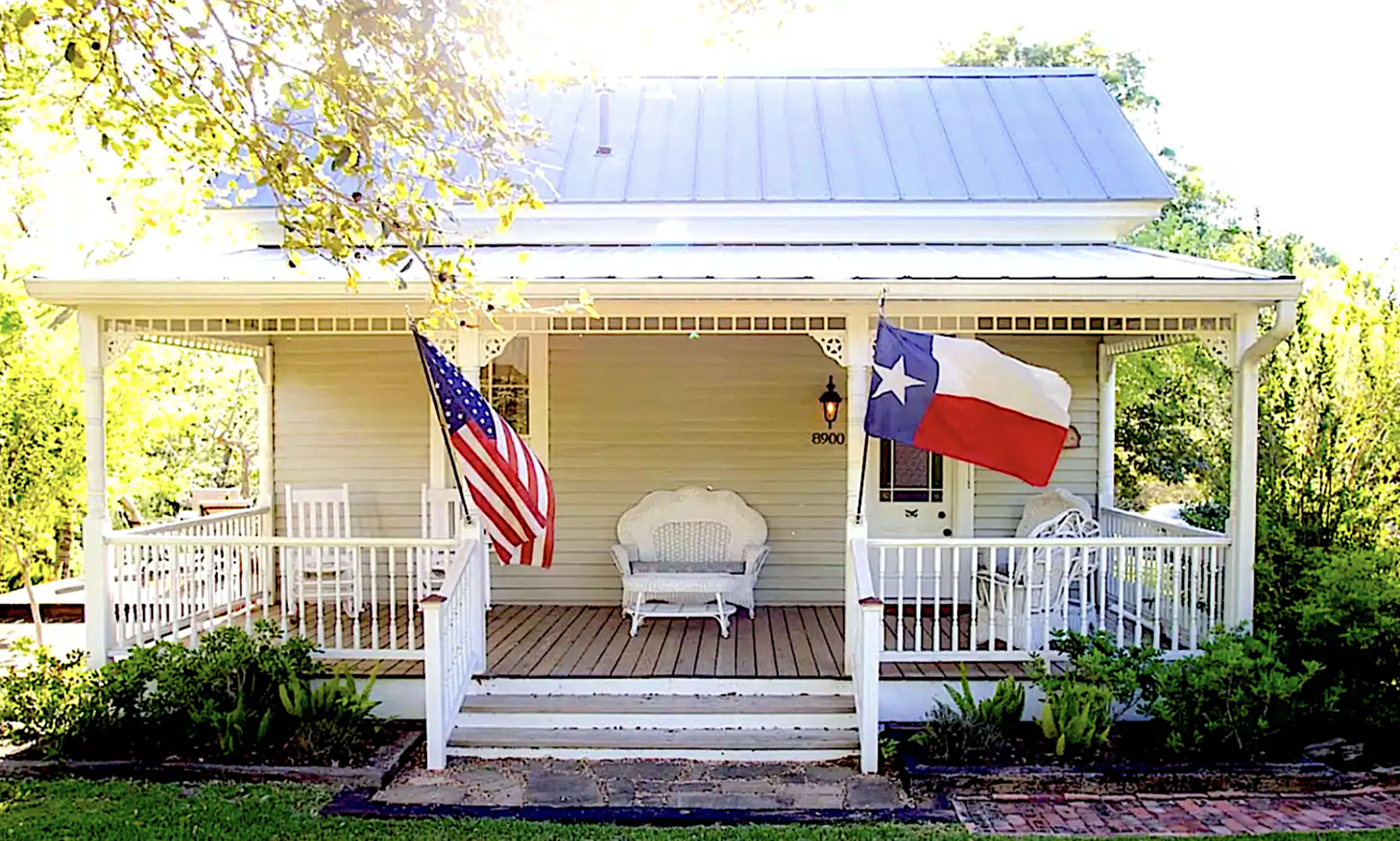 A house with a porch displays an American flag and a Texas state flag.