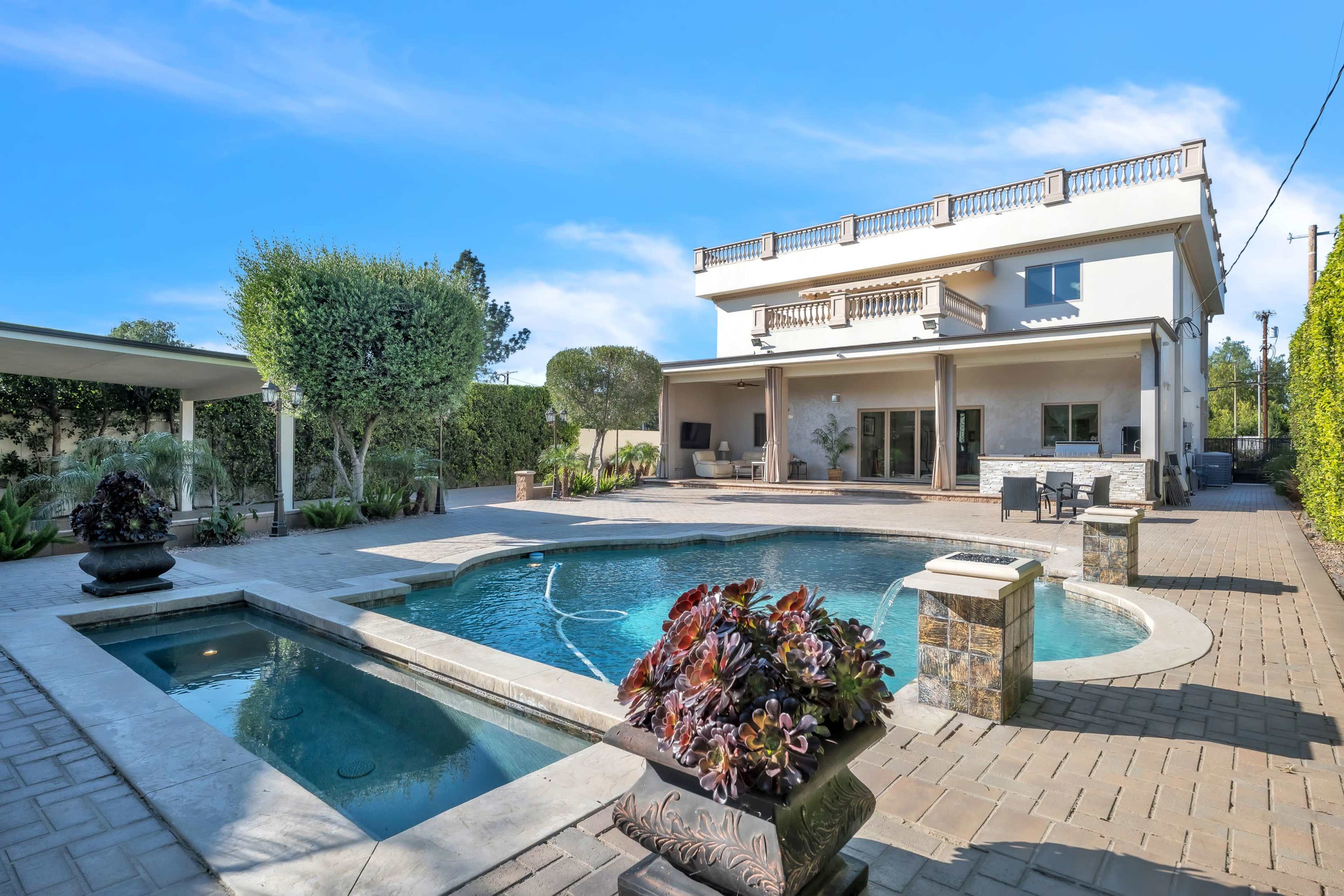 The image shows a large backyard featuring a pool, spa, and a two-story house with outdoor seating.