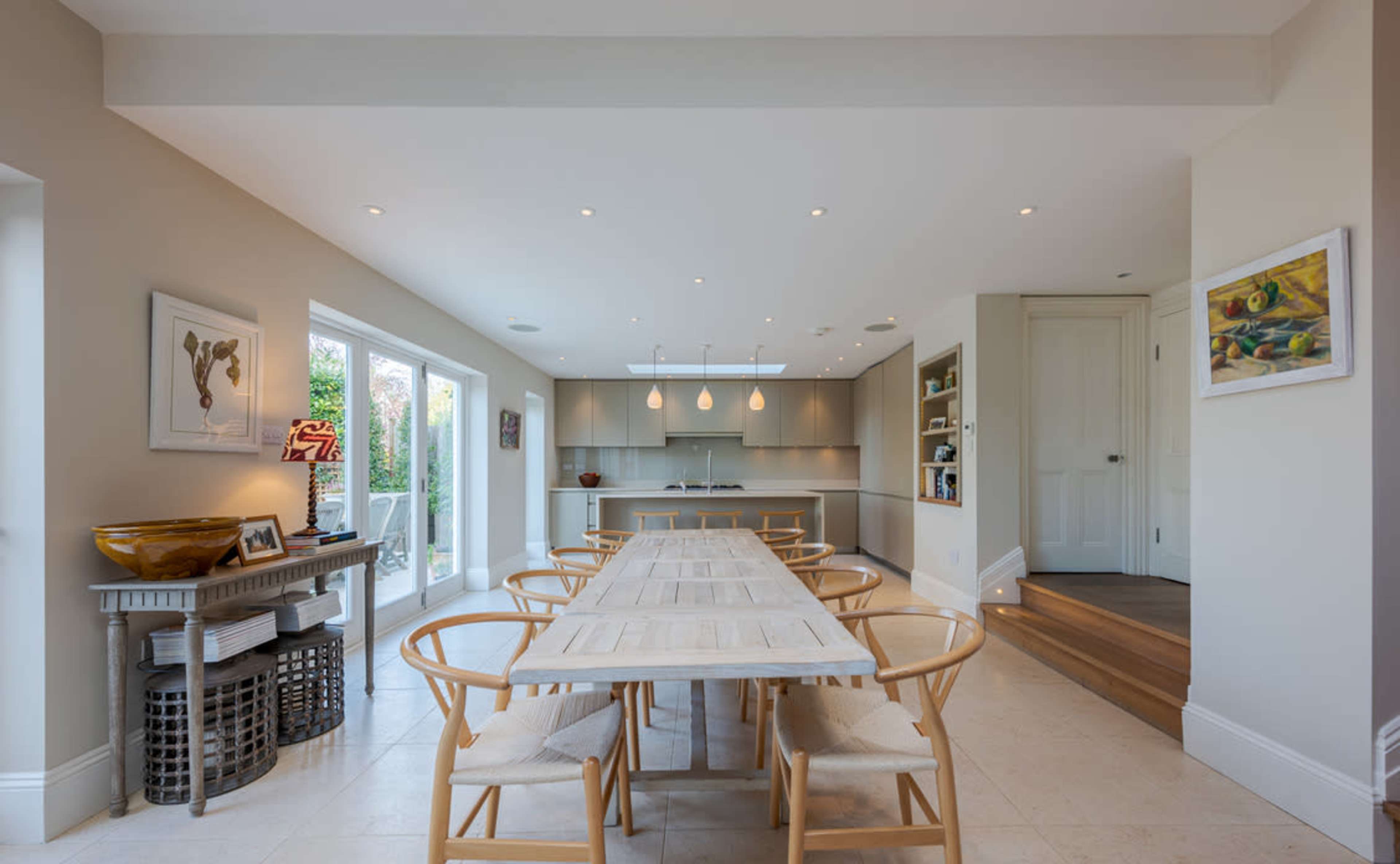 A modern kitchen and dining area with a long table, light-colored cabinetry, and sliding glass doors leading to an outdoor space.