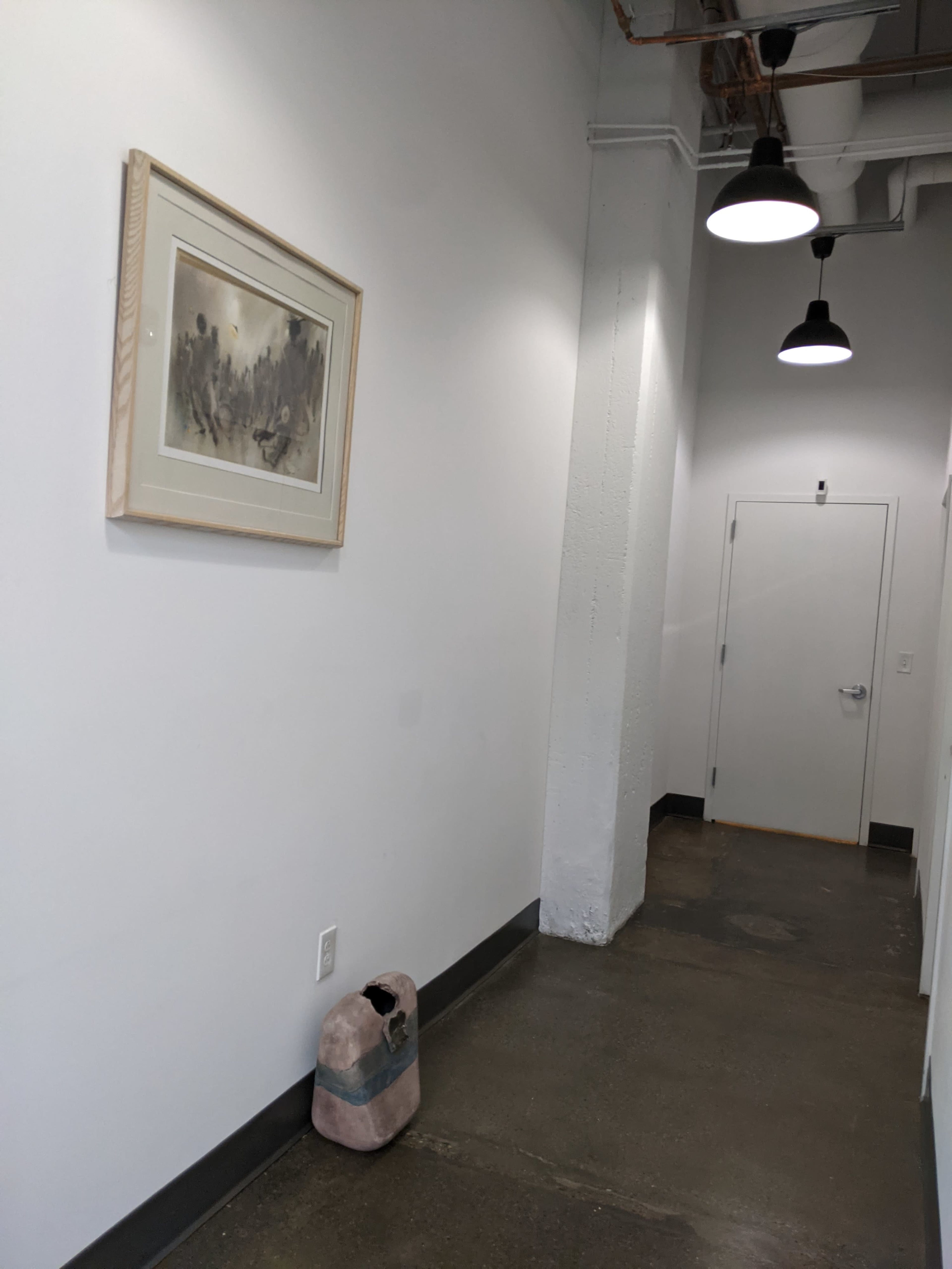 A narrow hallway features a framed artwork on the wall, a door at the end, and a small, pink object on the floor.