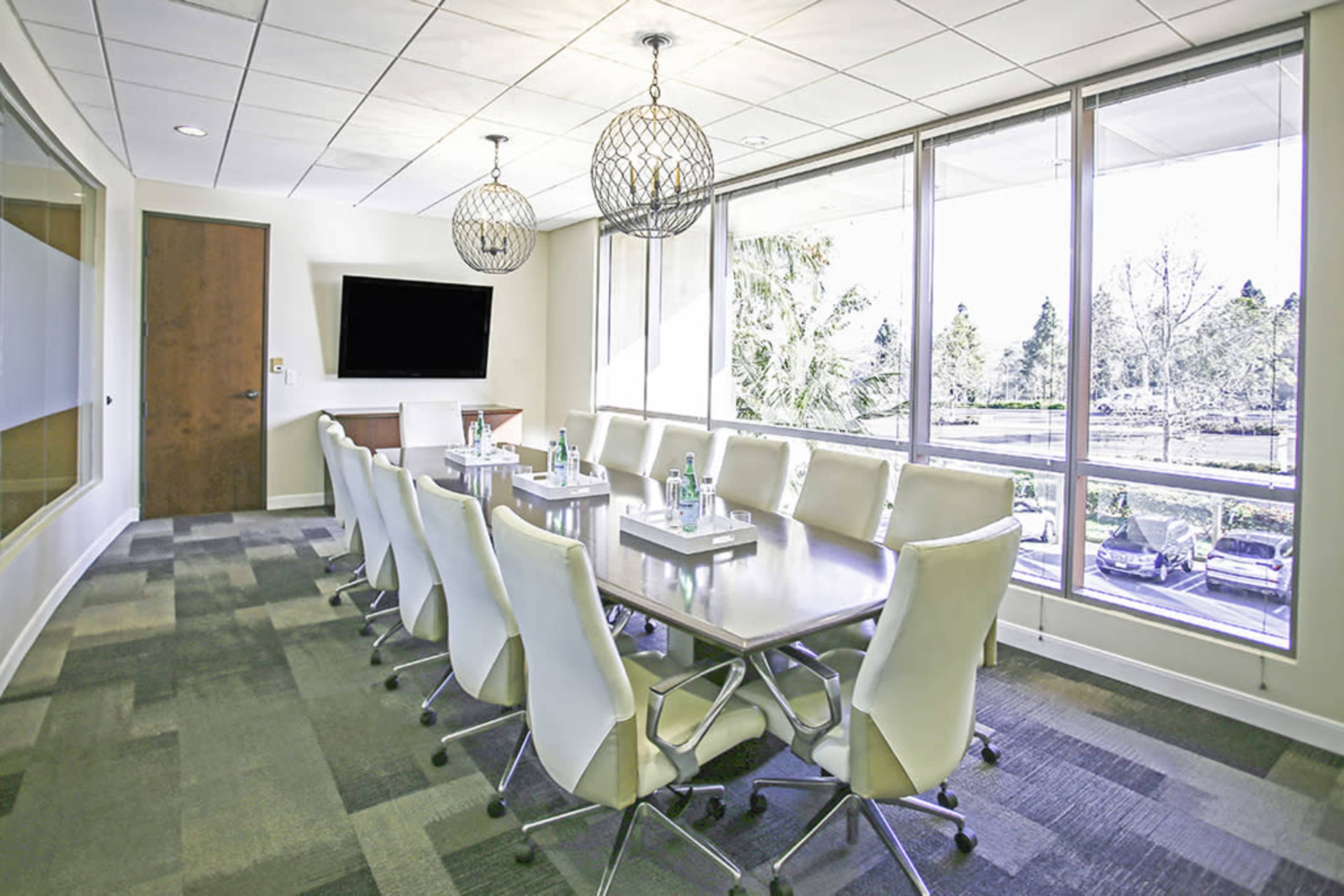 The image shows a modern conference room with a long table, white ergonomic chairs, and large windows allowing natural light to enter.