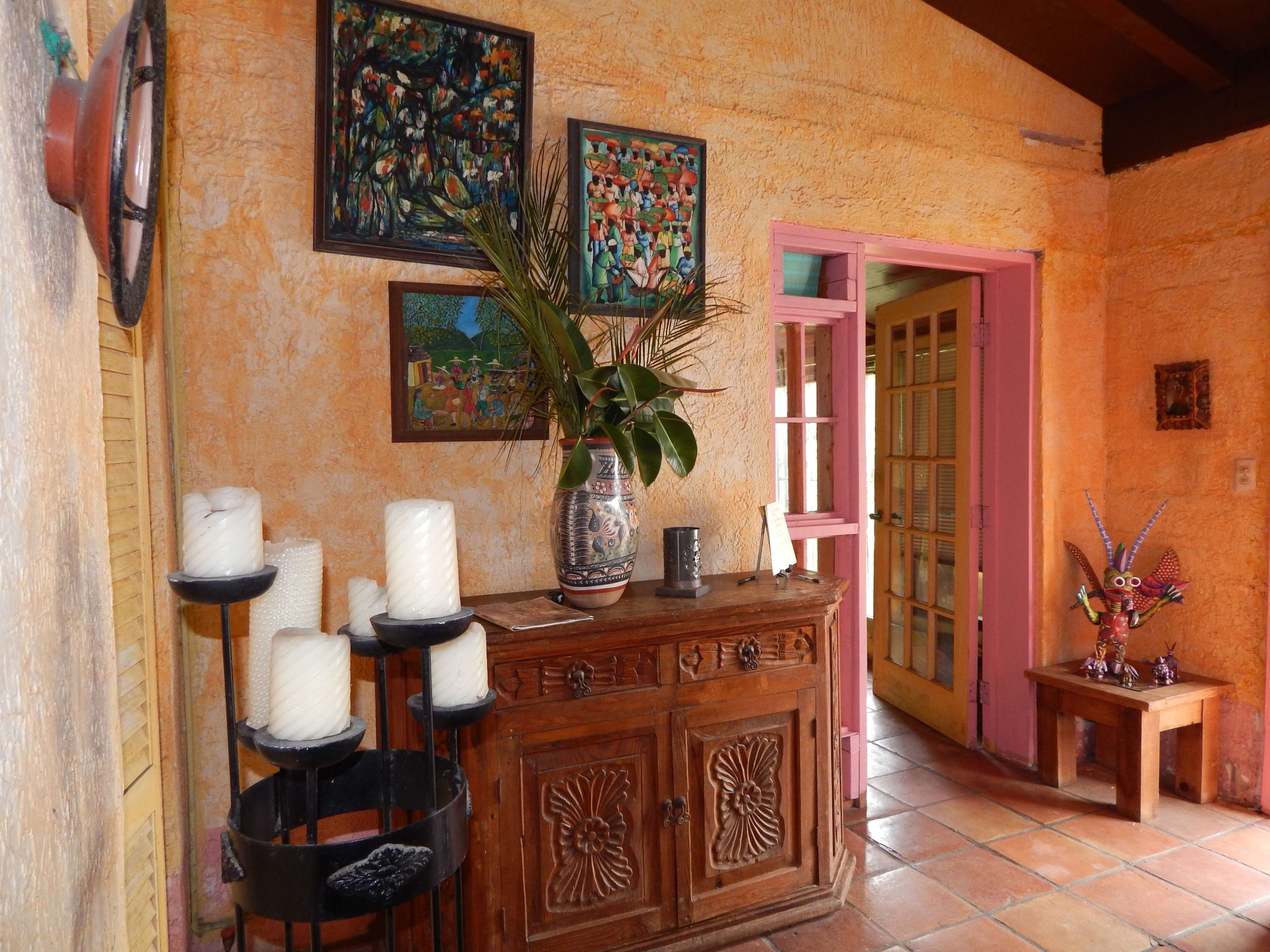 An interior room featuring a wooden cabinet with decorative items, various paintings on the walls, and a doorway leading to another room.