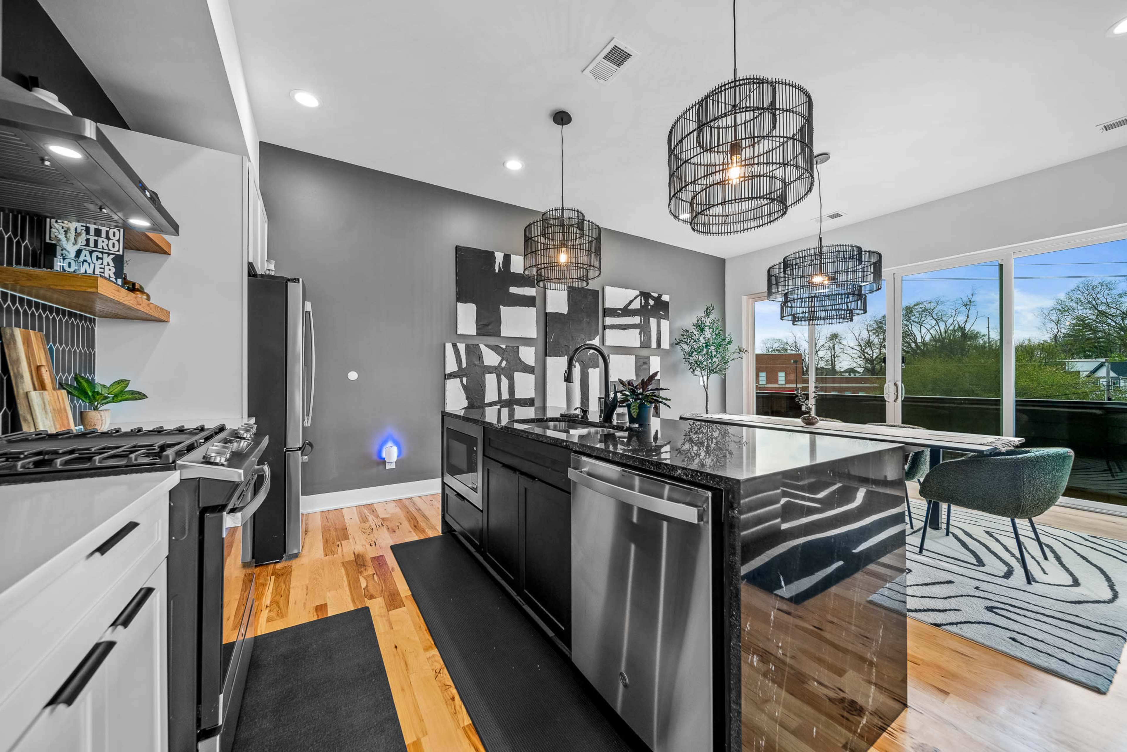 A modern kitchen features a central island with a black countertop, sleek appliances, and large windows overlooking a deck.