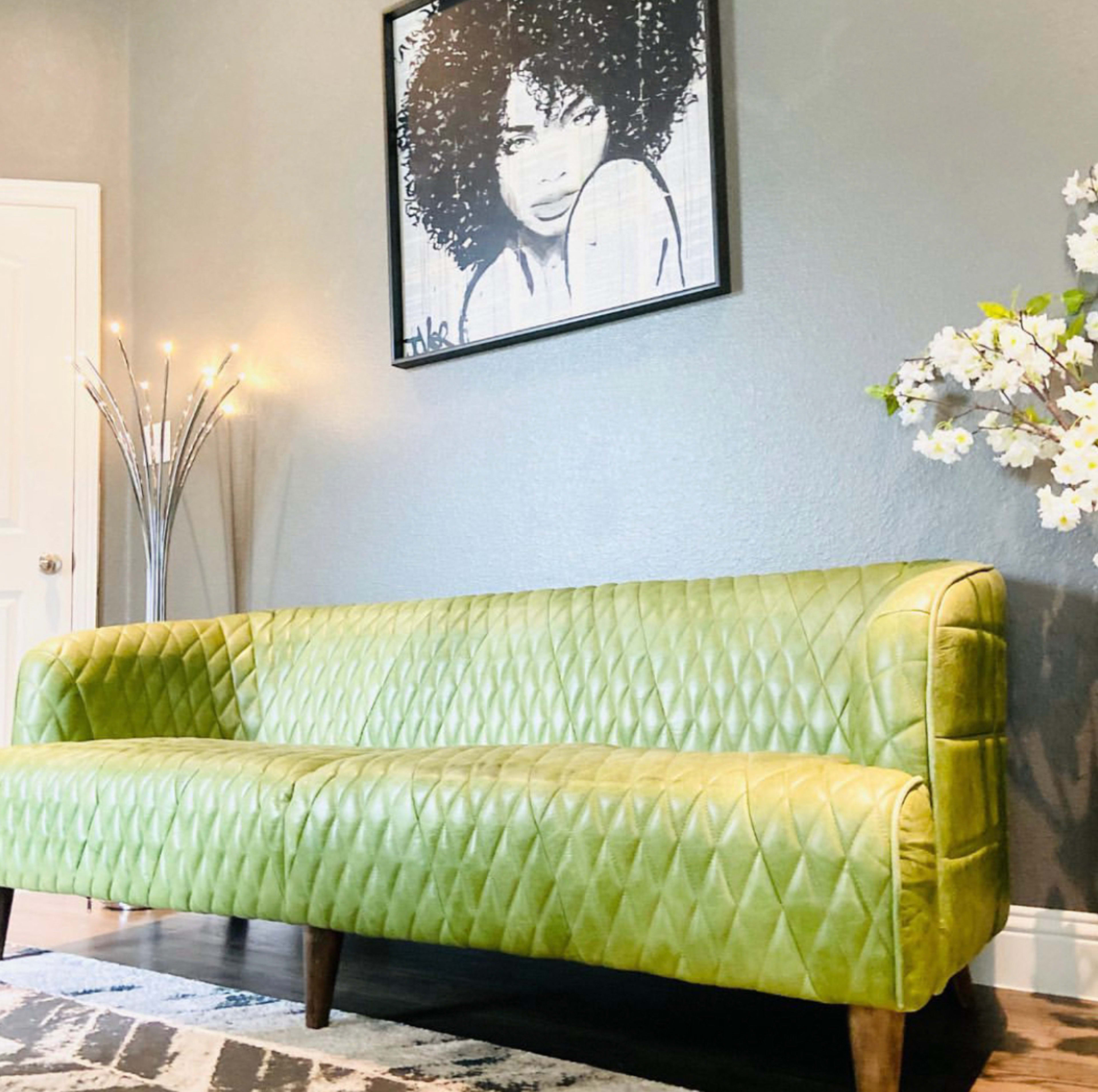 The room features a green upholstered sofa with diamond stitching and a framed artwork of a woman with curly hair on the wall above it.