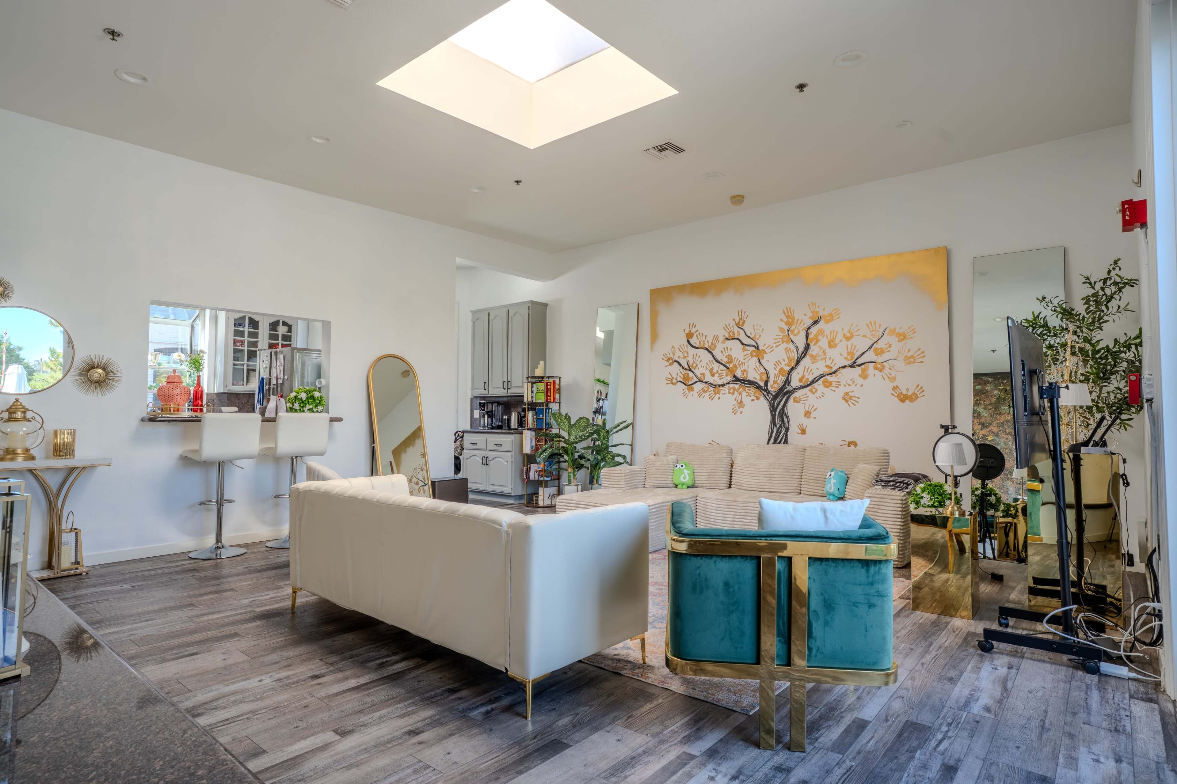 The image shows a modern living room with a white sectional sofa, a turquoise accent chair, and a large artwork of a tree on the wall.