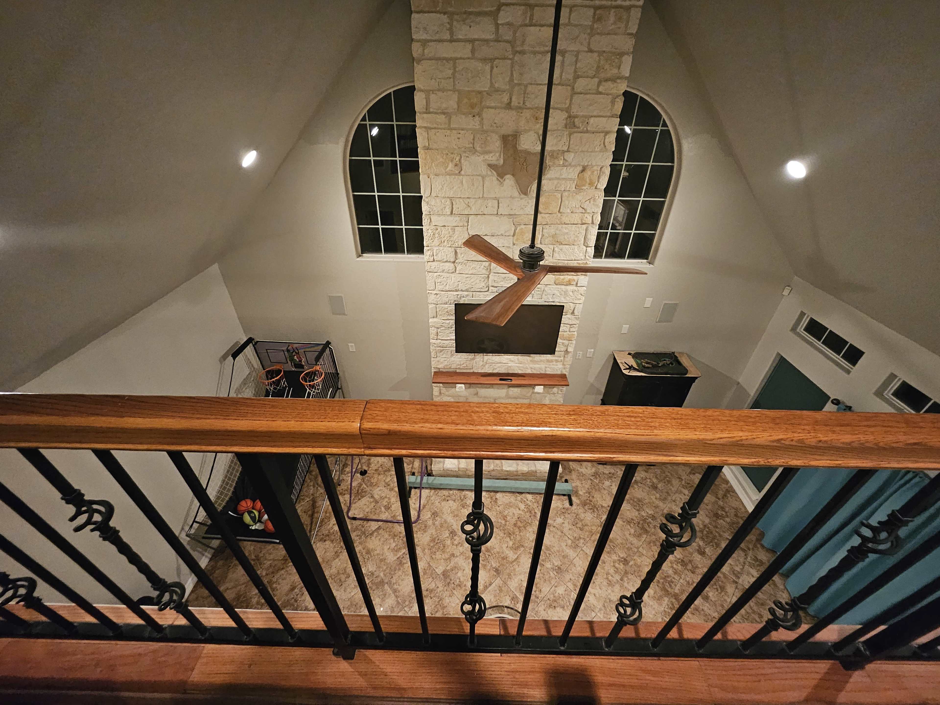 The image shows an interior view of a spacious living room with a stone fireplace and large windows, as seen from an upper balcony.
