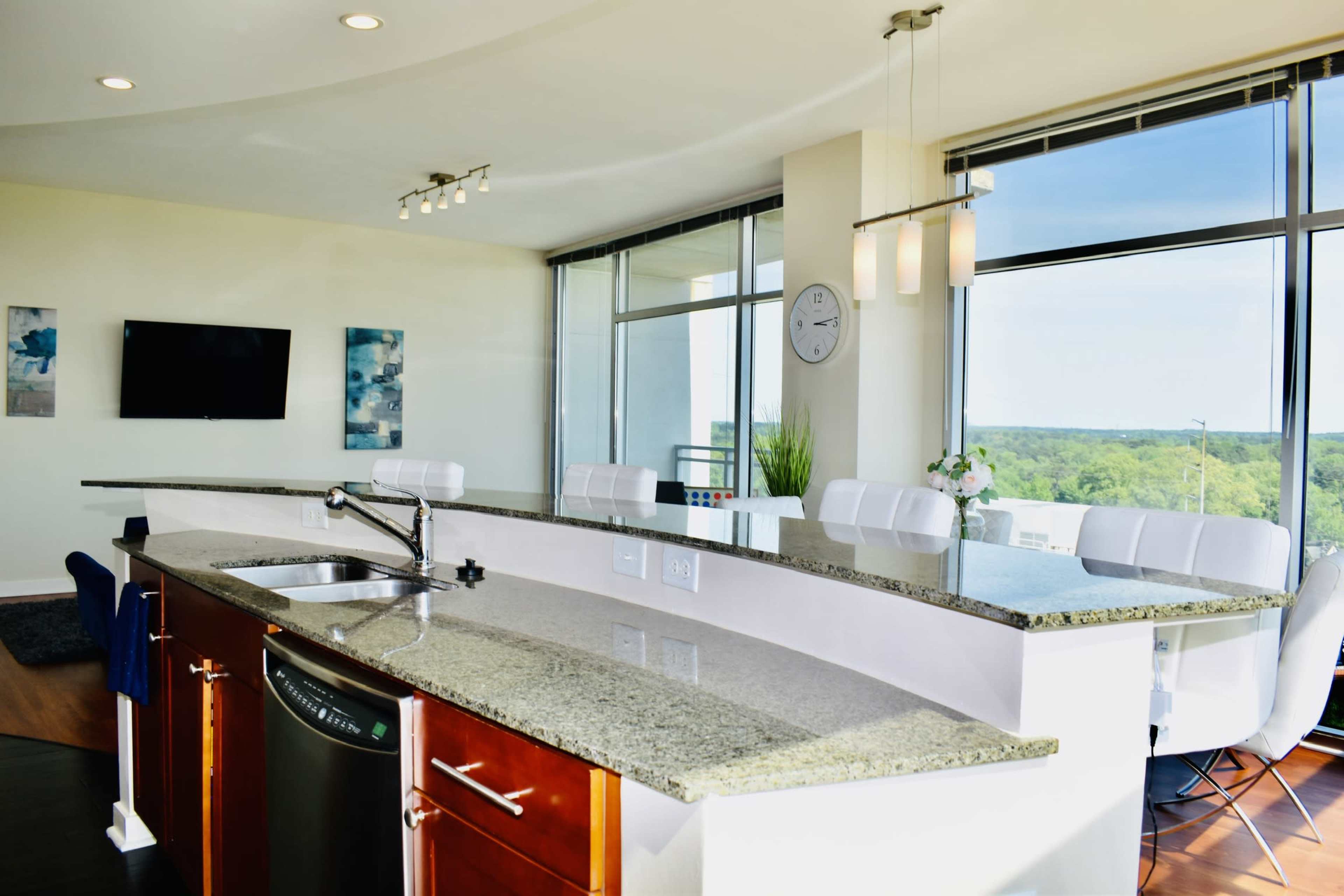 A modern kitchen features a granite countertop with a sink and a bar area, overlooking a scenic view through large windows.