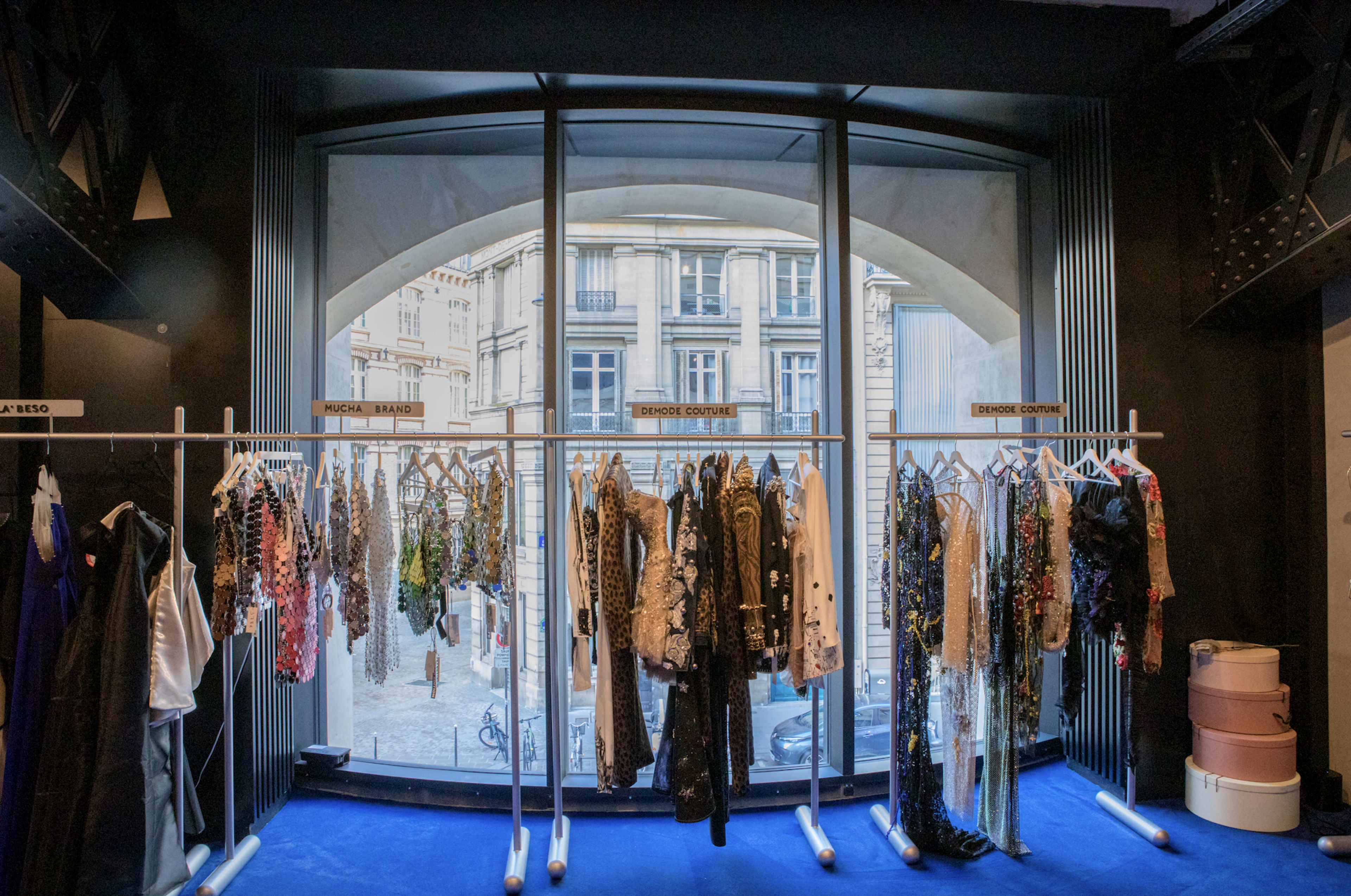 A clothing display in a boutique features racks of garments in front of a large window overlooking a city street.