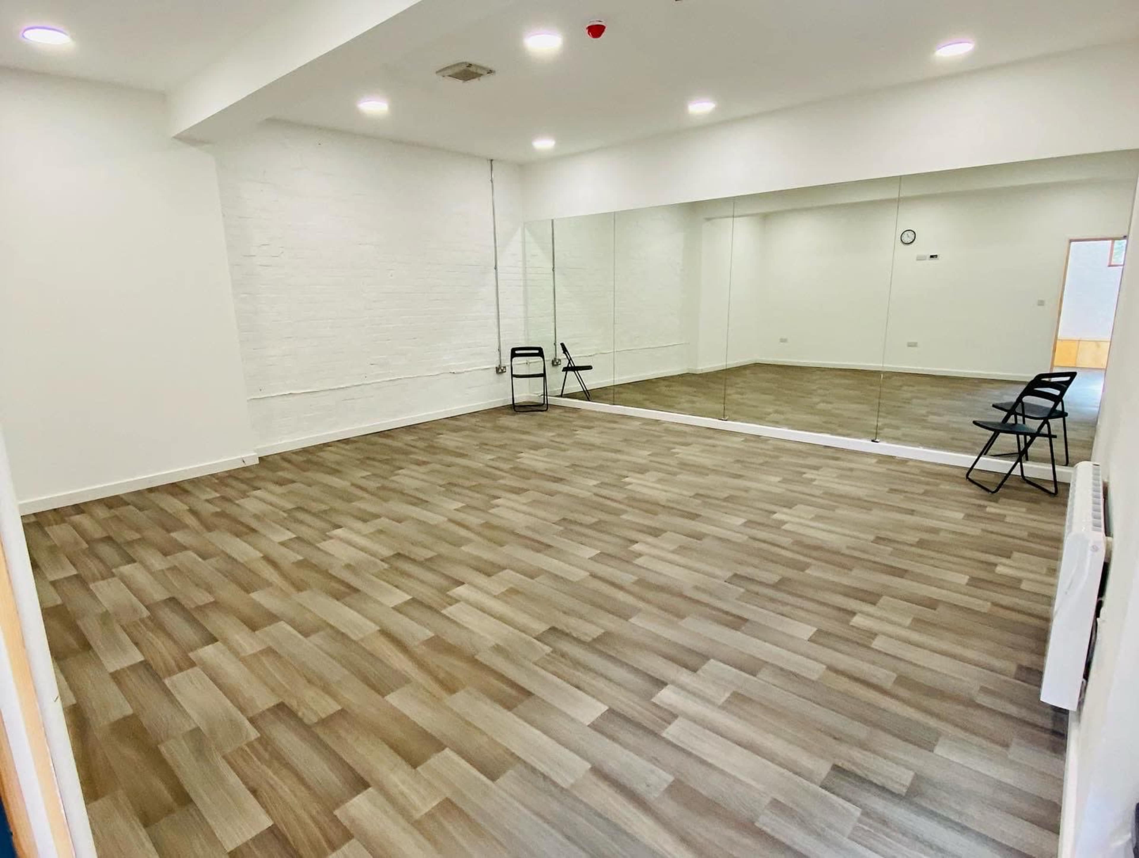An empty room with wooden flooring, white walls, and a large mirror on one side.