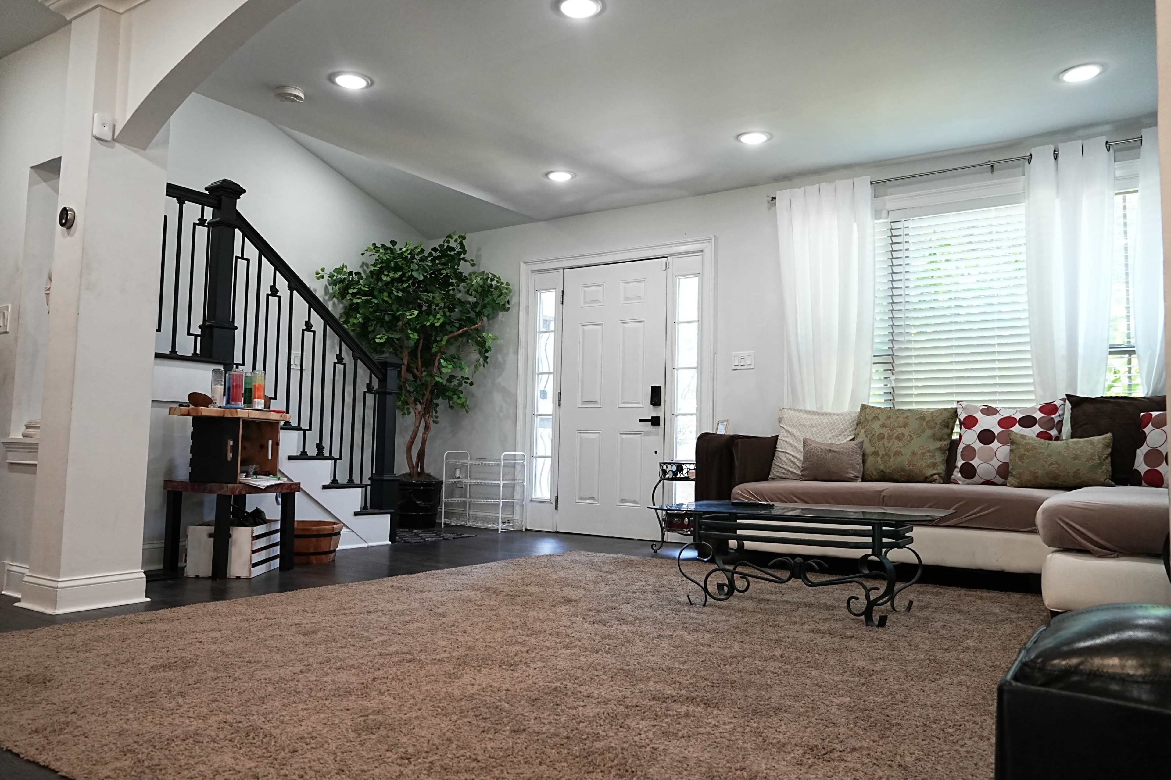 A living room with a couch adorned with decorative pillows, a coffee table in front, a staircase on the left, and a door leading outside.