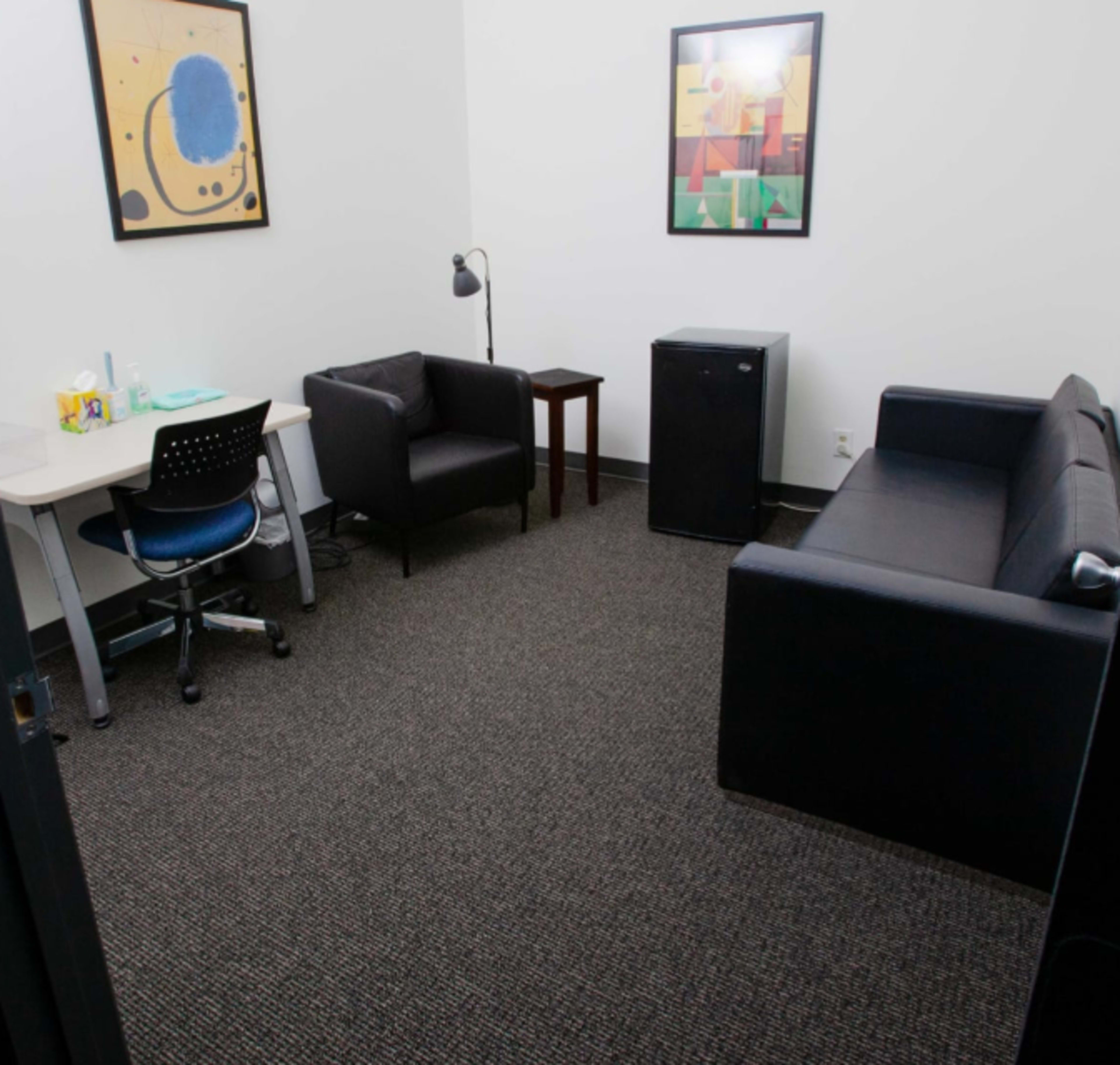 A small, furnished office space with a desk, two armchairs, a couch, and a small refrigerator.