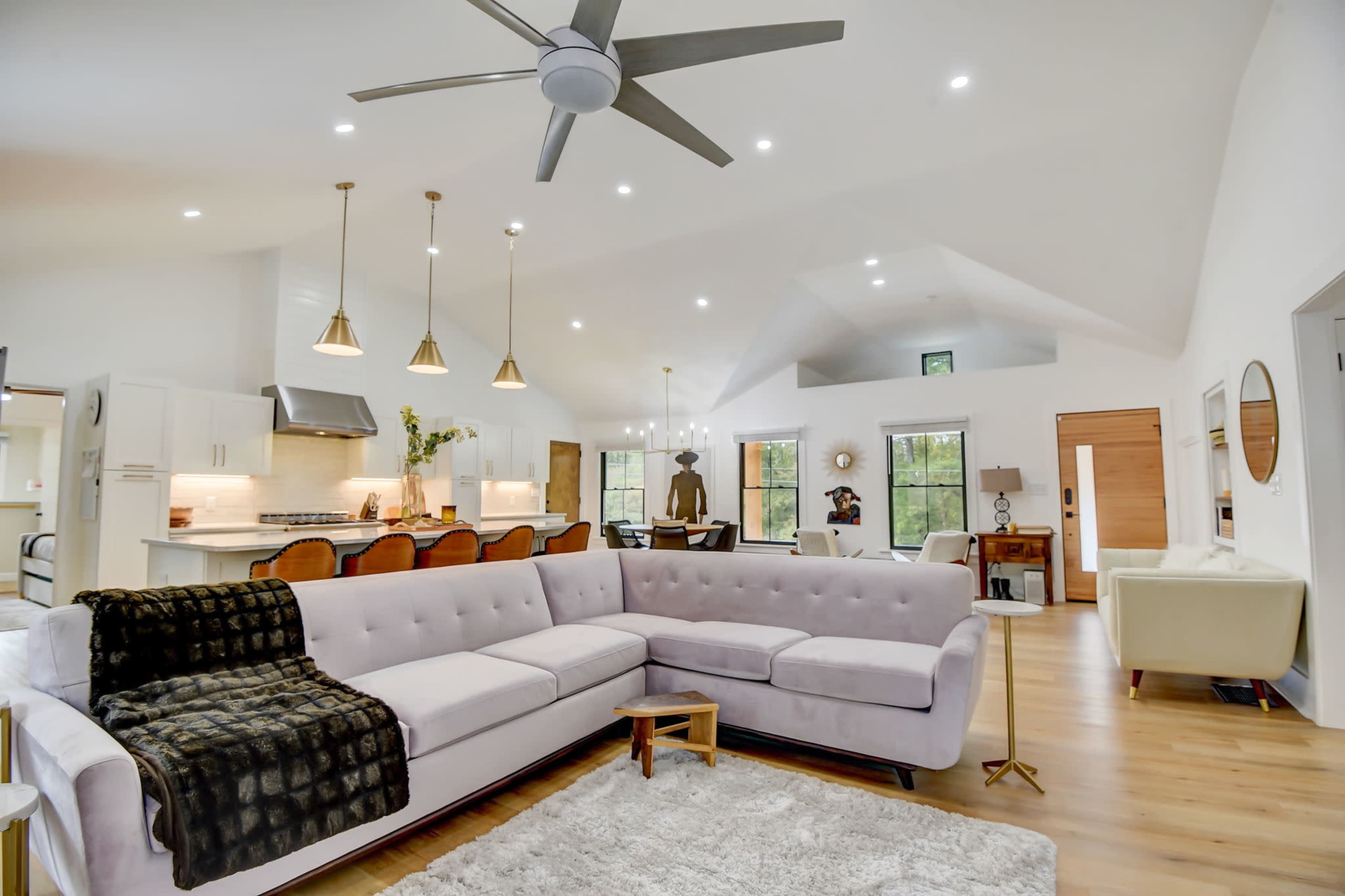 A modern living room features a large sectional sofa, a dining area, and an open-concept kitchen illuminated by pendant lighting.