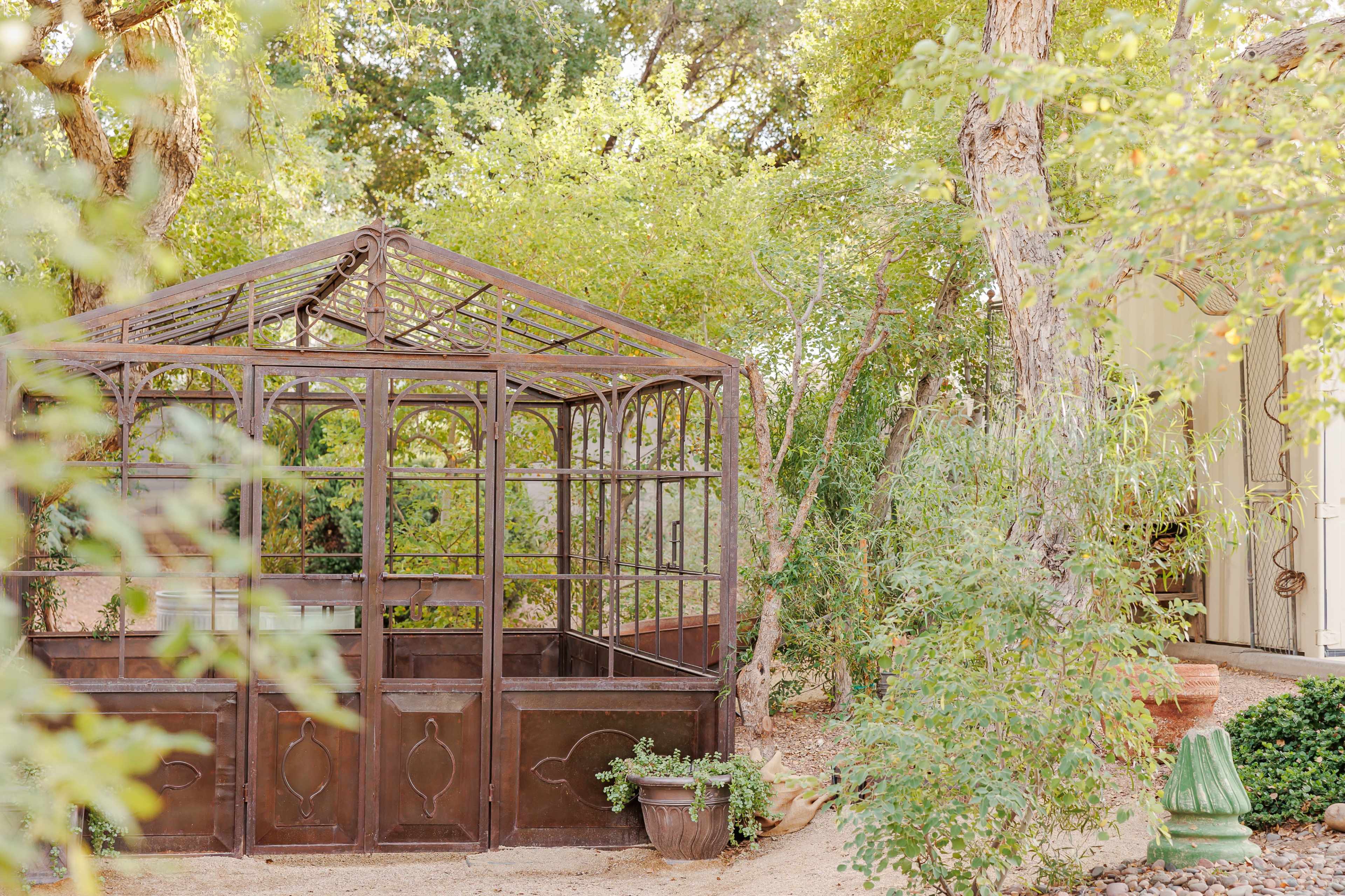 A metal-framed greenhouse is situated among lush greenery.