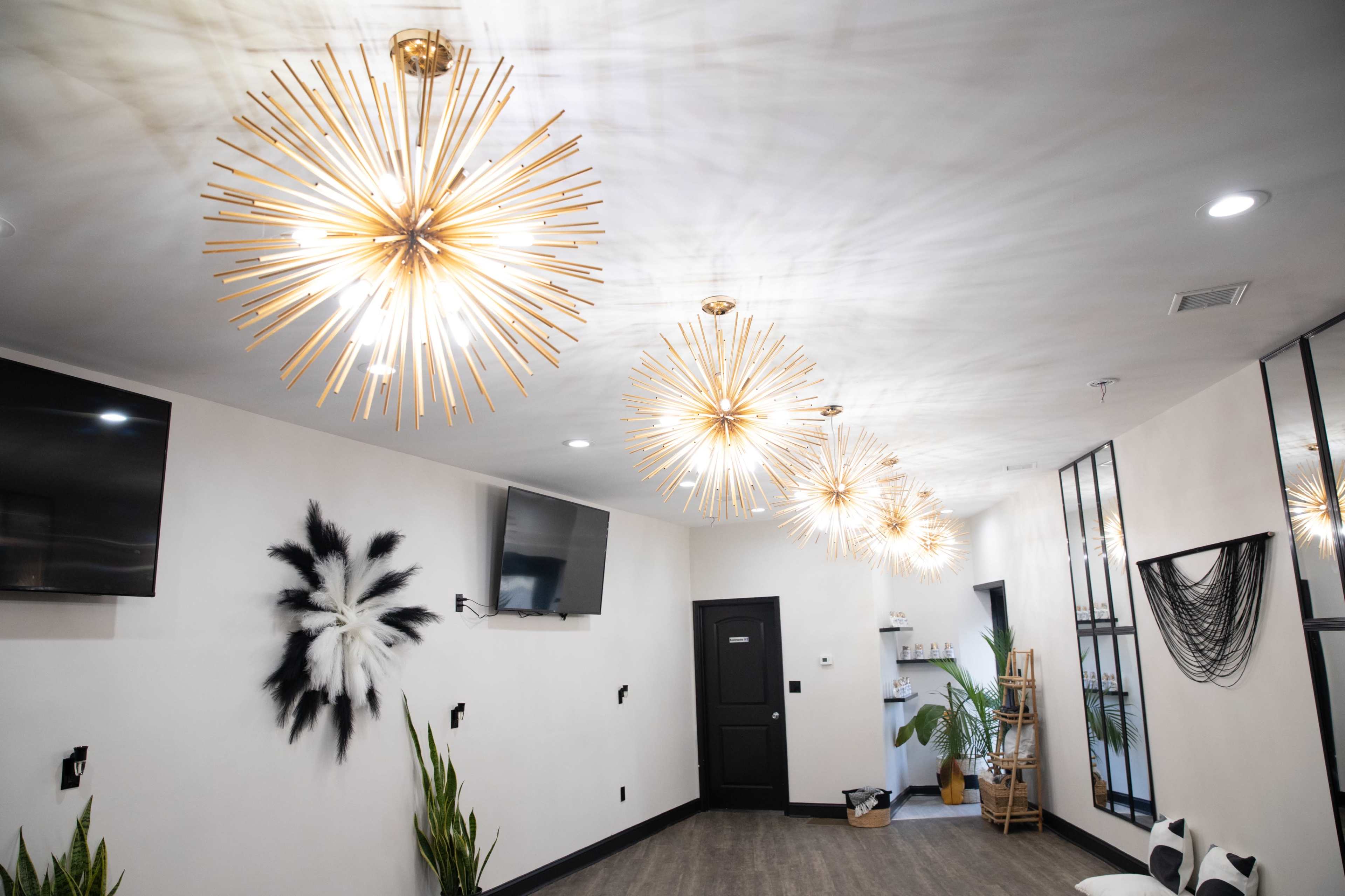 A modern interior space with four starburst pendant lights hanging from the ceiling, black and white wall decor, and plants in the corners.