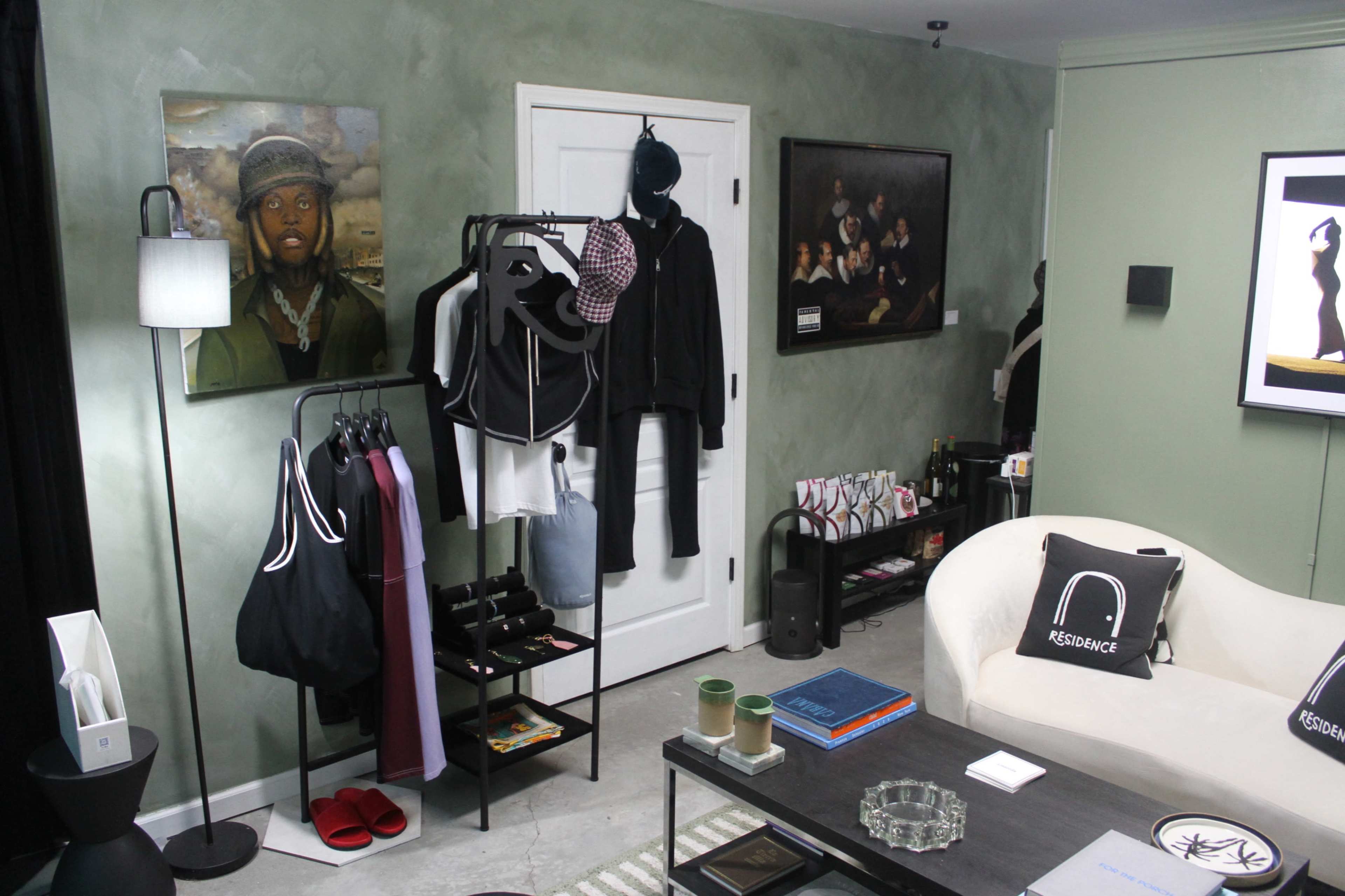 The image shows a modern interior space featuring a clothing rack with various garments, a black and white sofa, and artwork on the walls.
