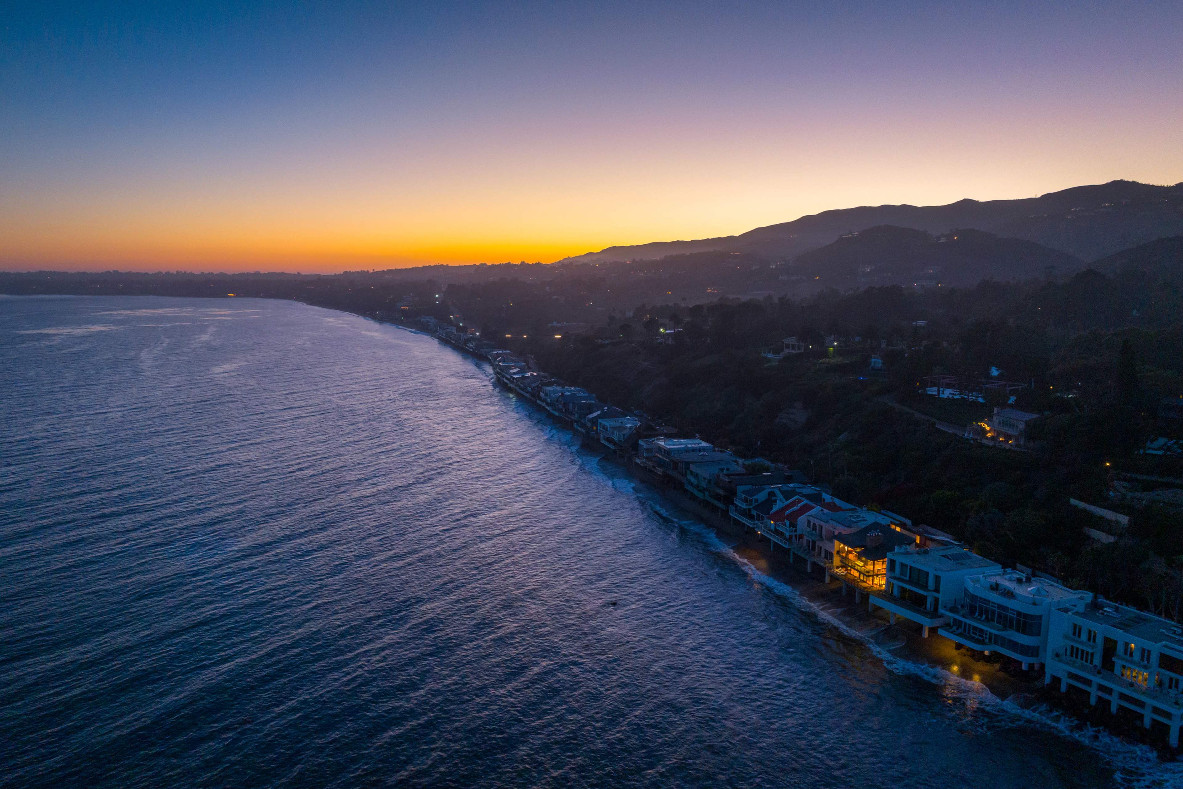 A coastal view at dusk, featuring houses along the shoreline with a sunset gradient in the sky.