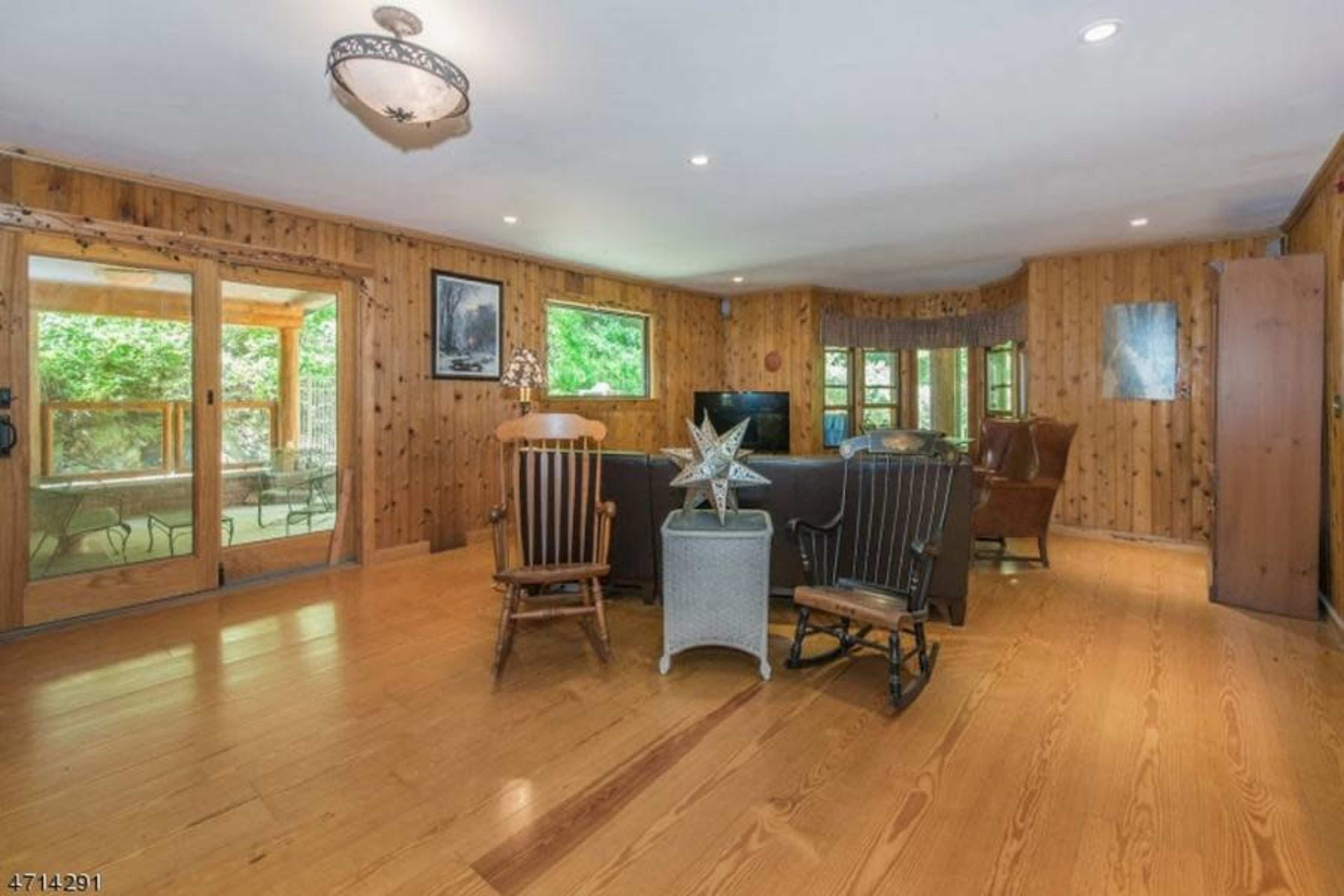 The room features wooden walls and flooring, with a seating area that includes two rocking chairs and a sofa, illuminated by natural light from large windows.