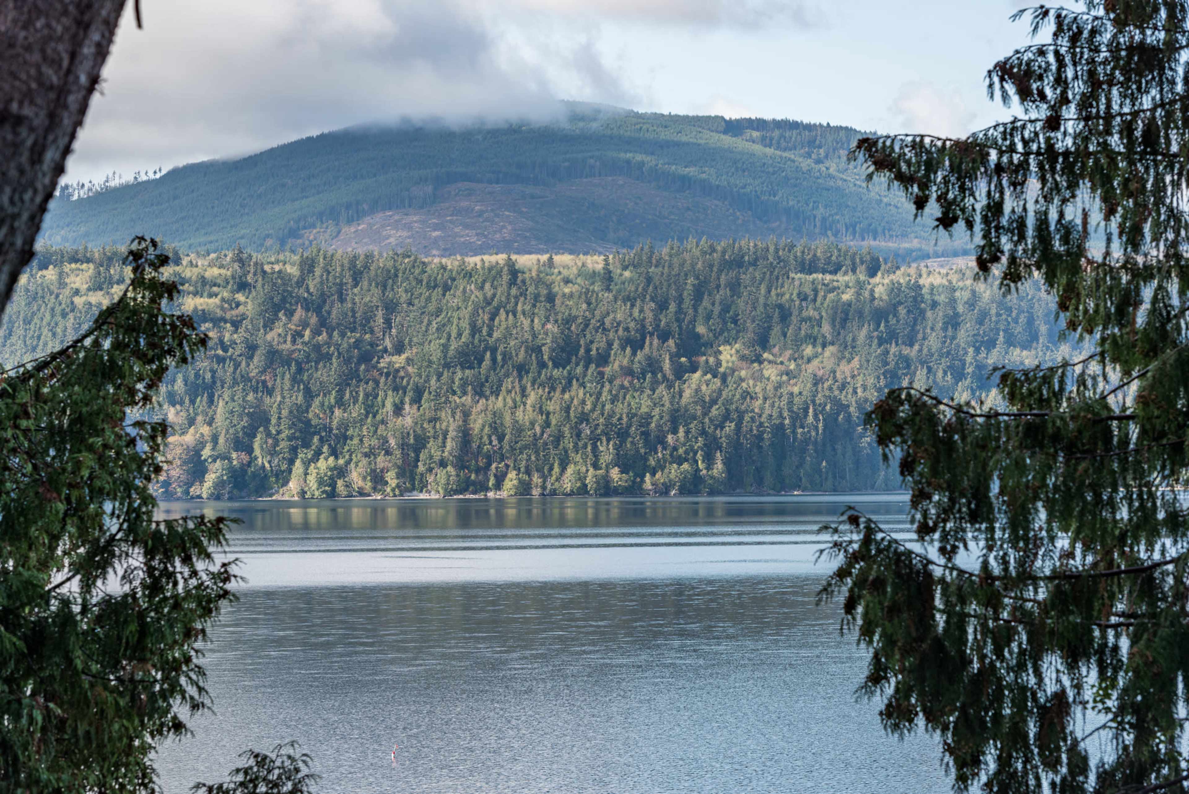 A calm lake reflects the surrounding forested hills under a partly cloudy sky.