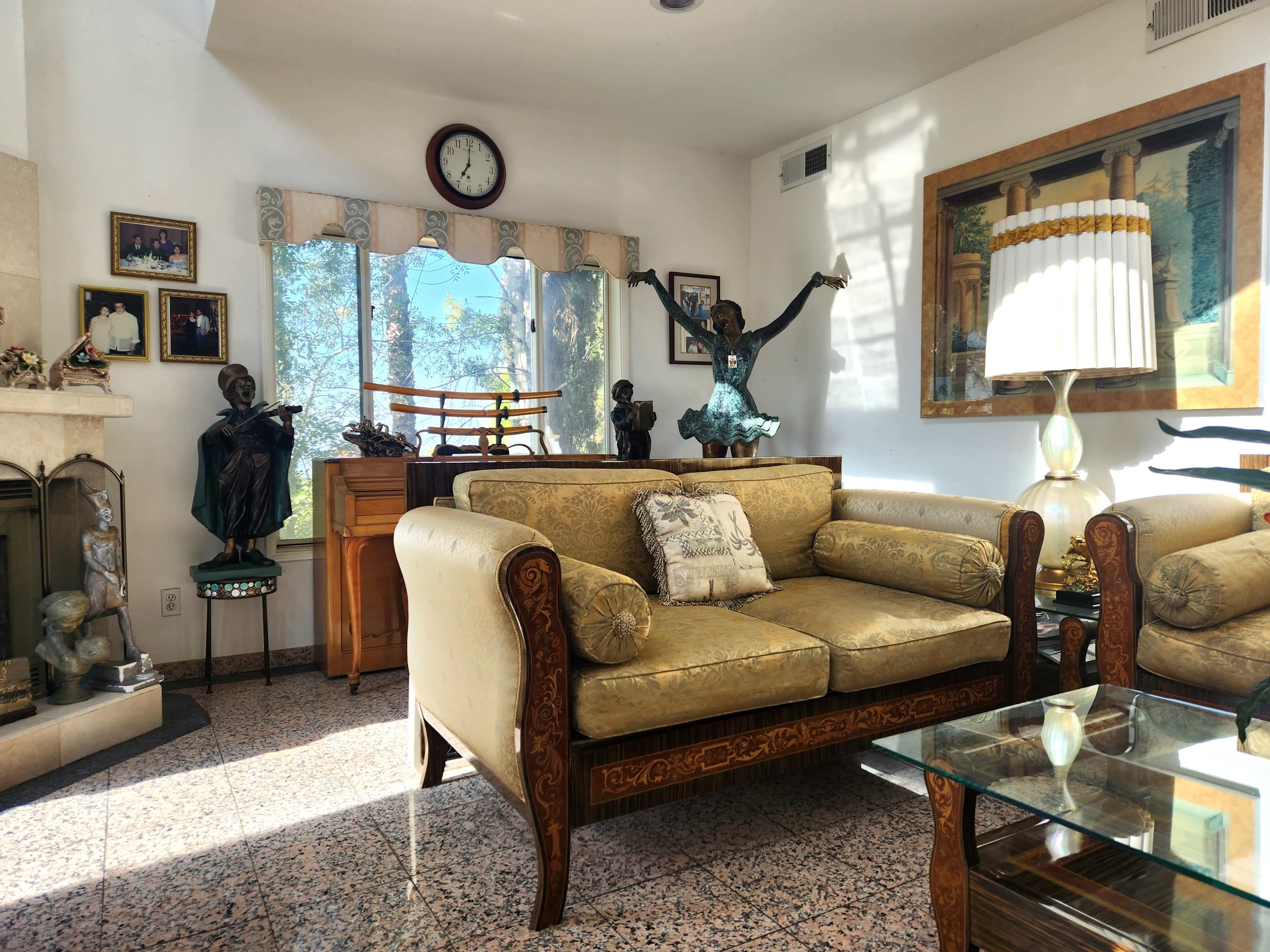 The living room features a yellow couch, a glass coffee table, a wooden chest, and several sculptures displayed on shelves and tables.