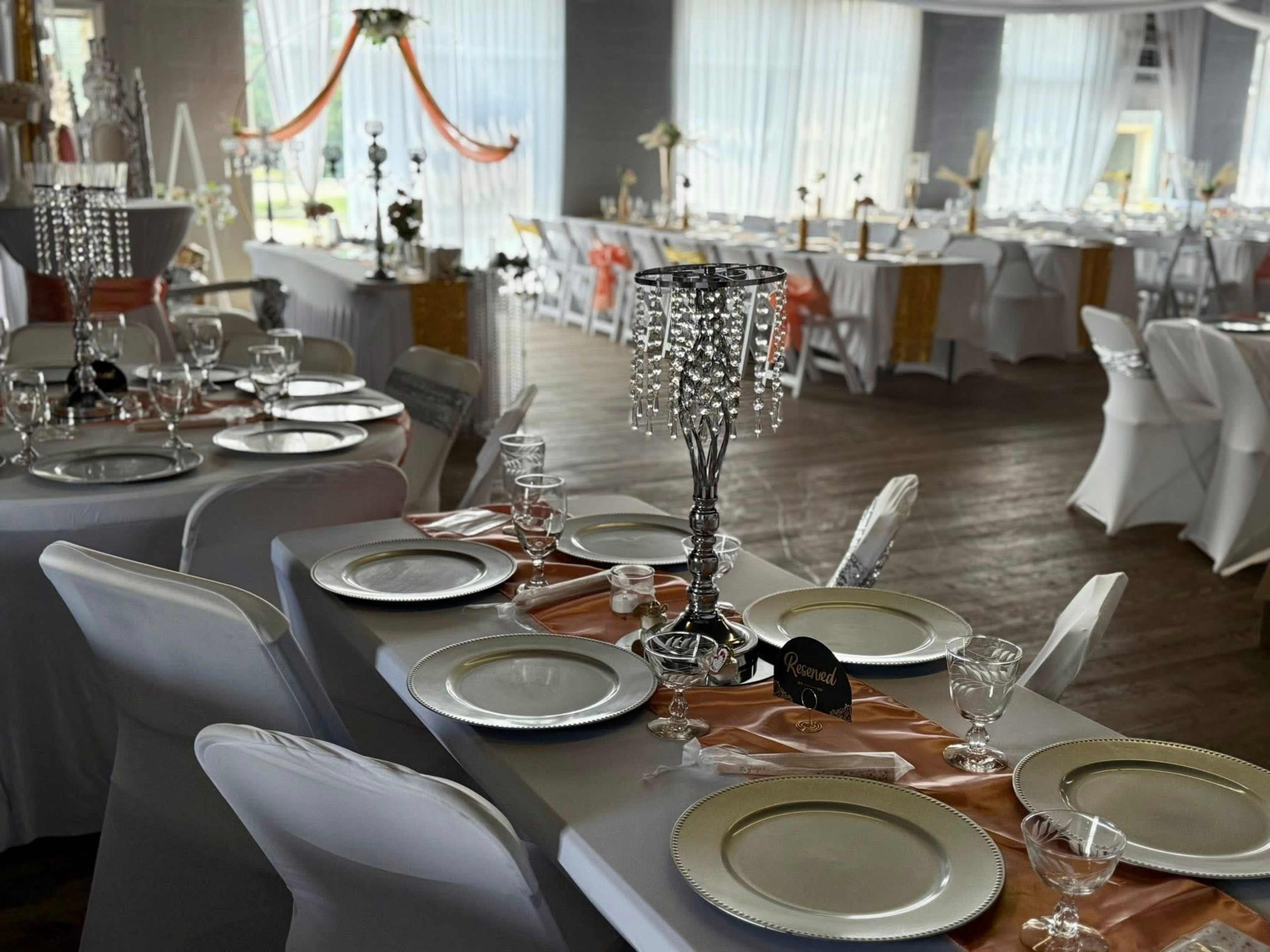 A banquet hall is set up for an event with elegantly arranged tables featuring white tablecloths, patterned plates, and decorative centerpieces.