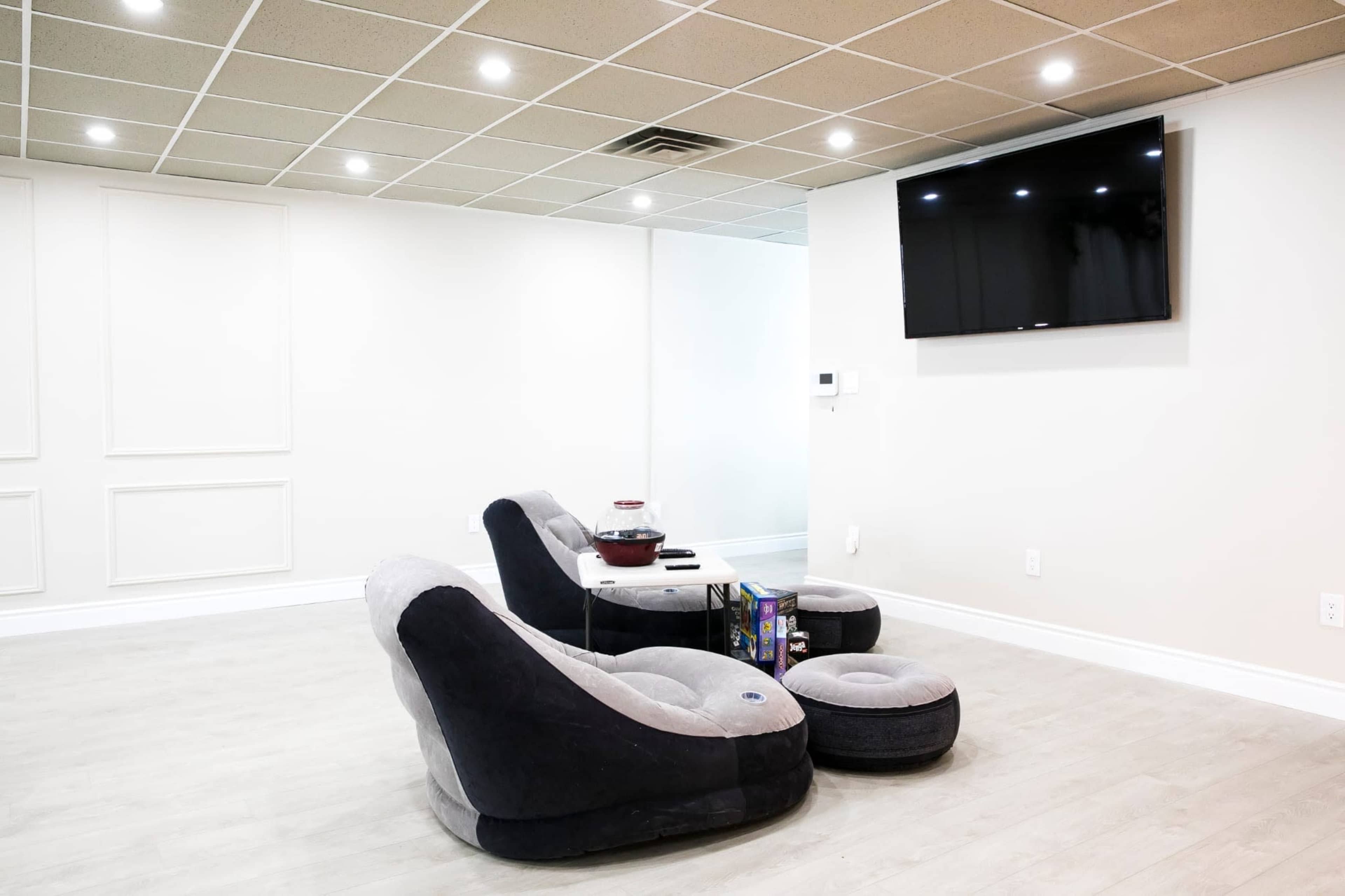 A modern lounge area with two curved chairs, a small table, and a flat-screen TV mounted on the wall, set against a light-colored backdrop.