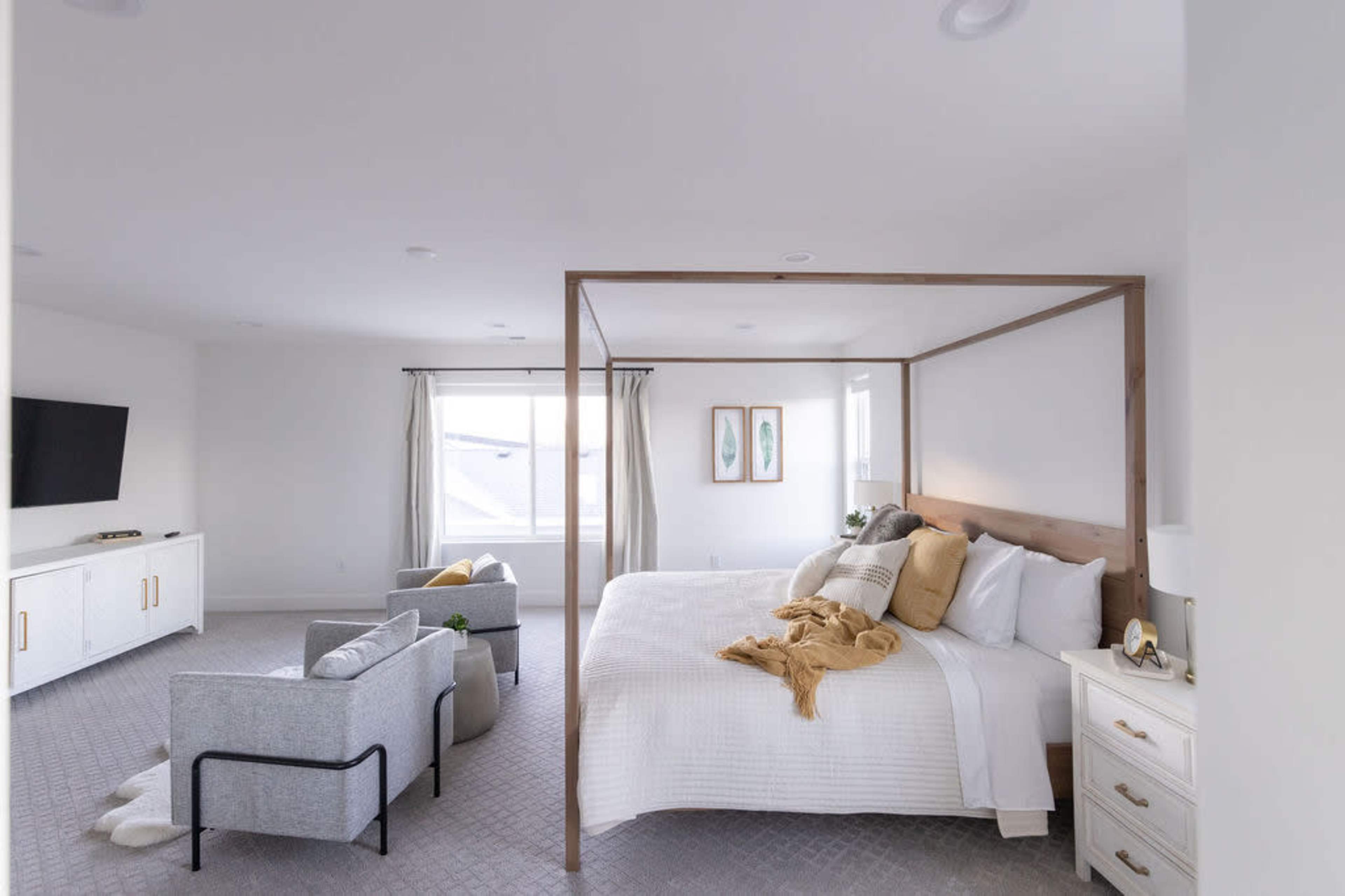 A spacious bedroom features a four-poster bed, a seating area with two chairs, and a large window with drapes.