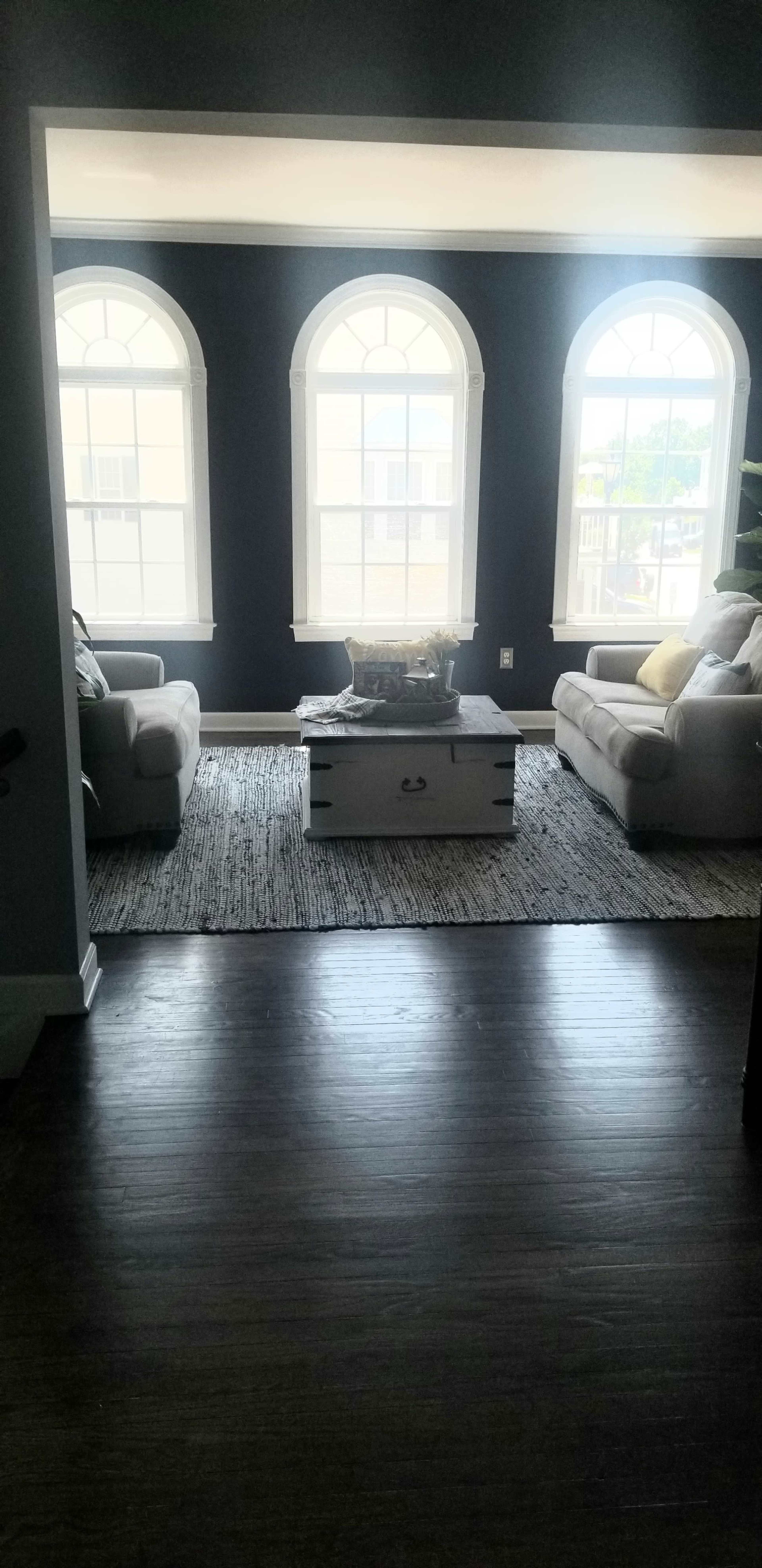 A living room features two light-colored sofas flanking a white coffee table, with large arched windows bringing in natural light.
