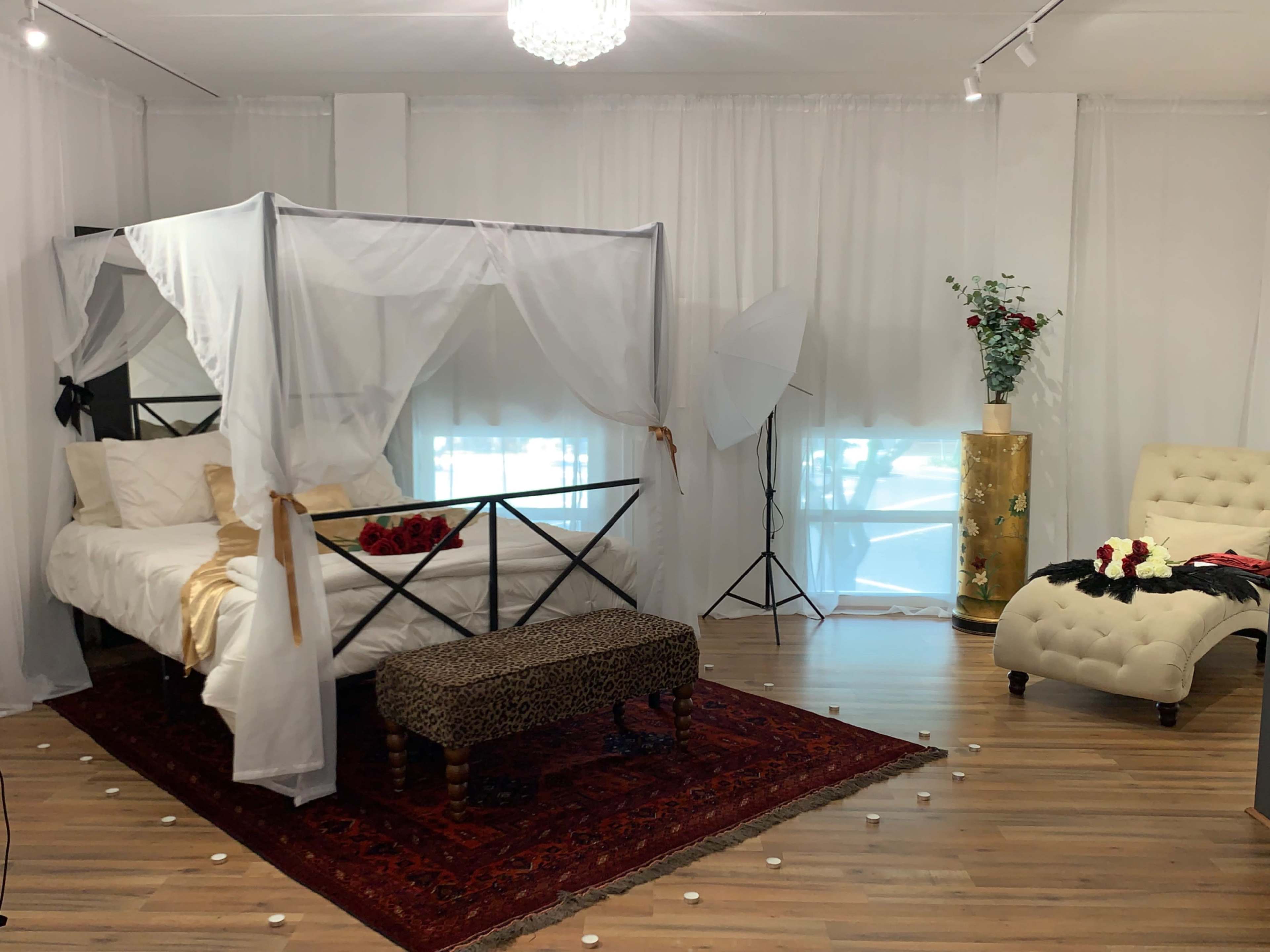 A styled bedroom features a canopy bed adorned with white drapes, a leopard-print bench, and romantic decorations scattered on the floor.