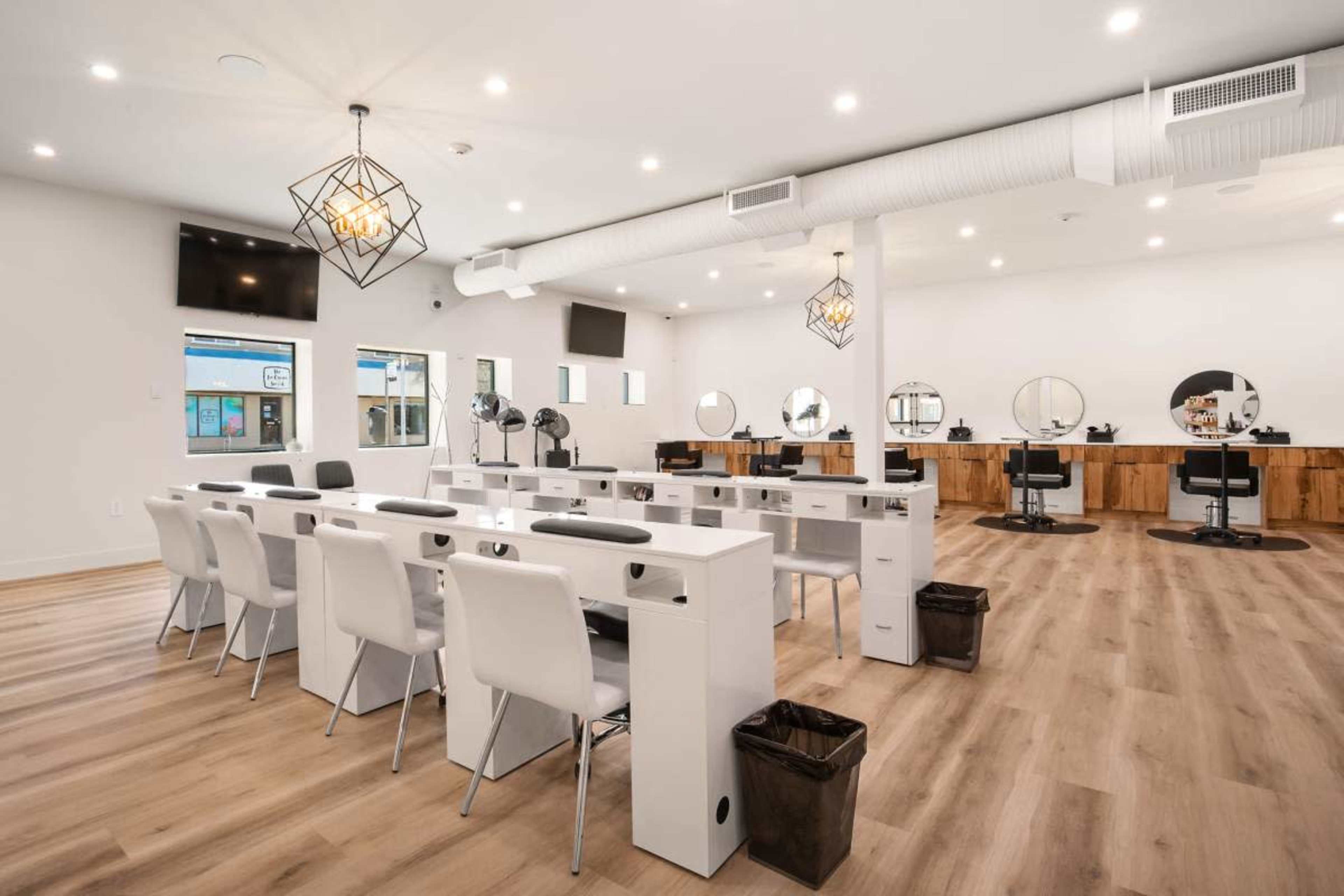 The image shows a spacious hair salon with white walls, wooden accents, multiple styling stations, and modern furniture arranged in a clean layout.